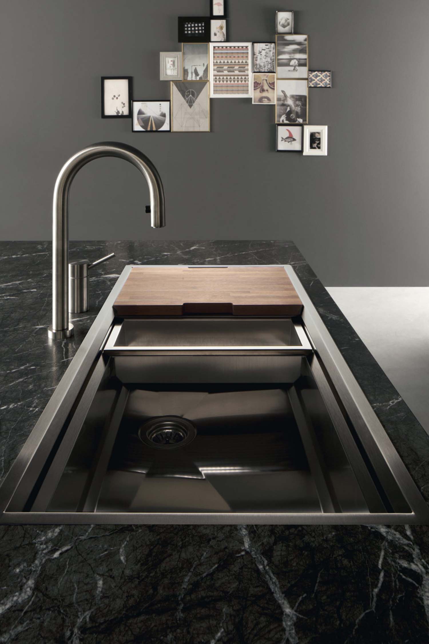 A contrasting stainless steel sink adds a jewel among the monochrome visual of factory. Additional elements slide up and down the perimeter of the sink for food preparation.