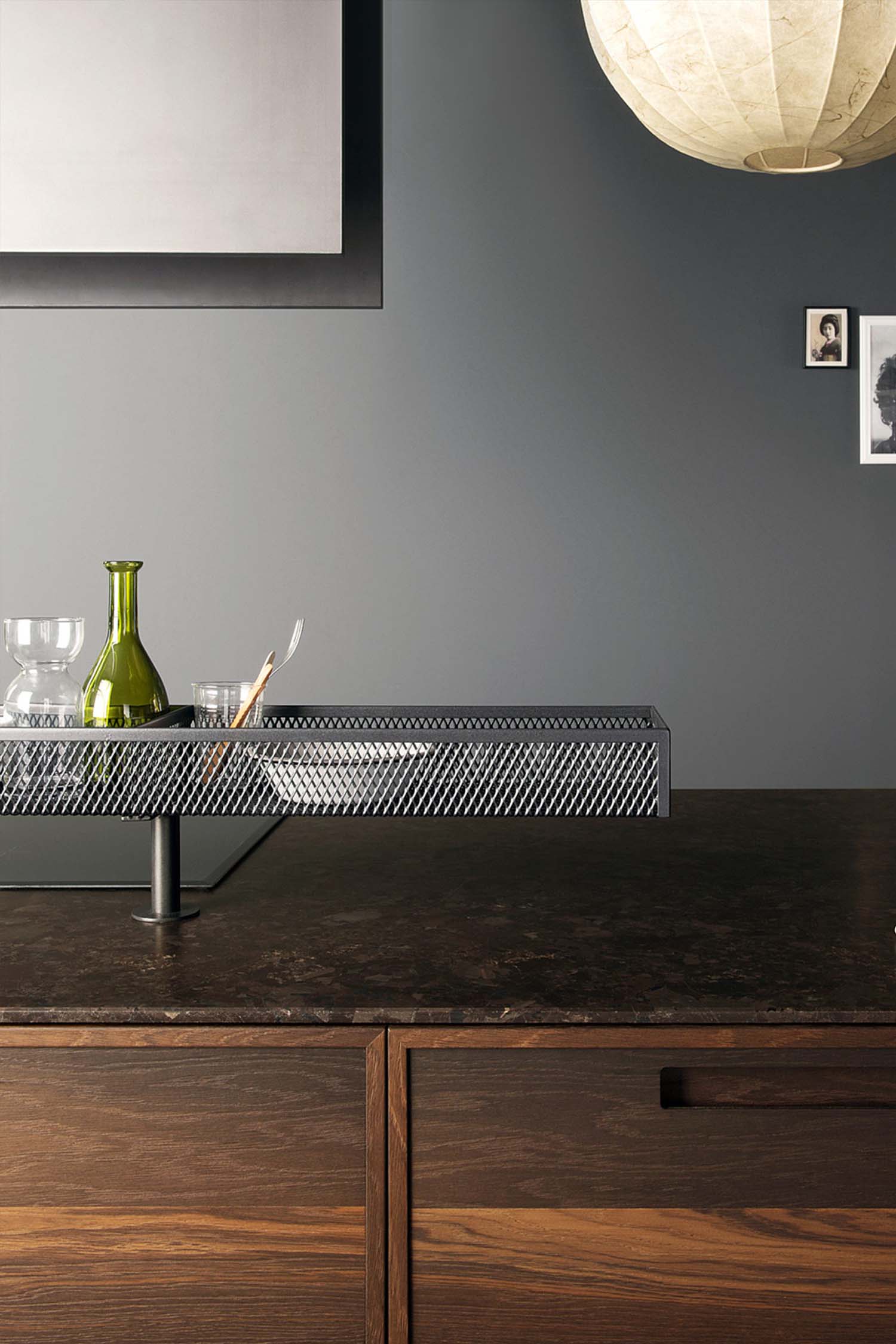 A detailed view of a black metal-framed wine rack and shelving unit. The unit is built into the kitchen wall and features integrated lighting. It holds various bottles and glasses, serving as both a functional storage solution and a stylish design element.