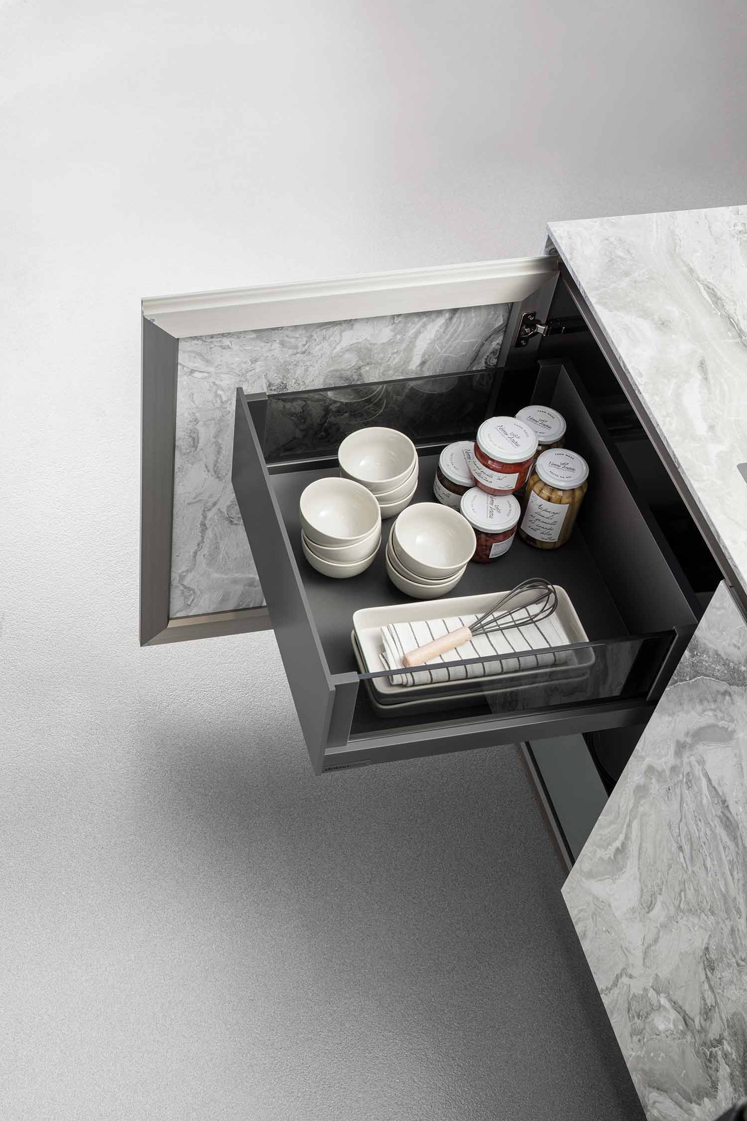 A detail of a handleless, black or dark grey kitchen drawer, with the light wood interior and its organizers visible.