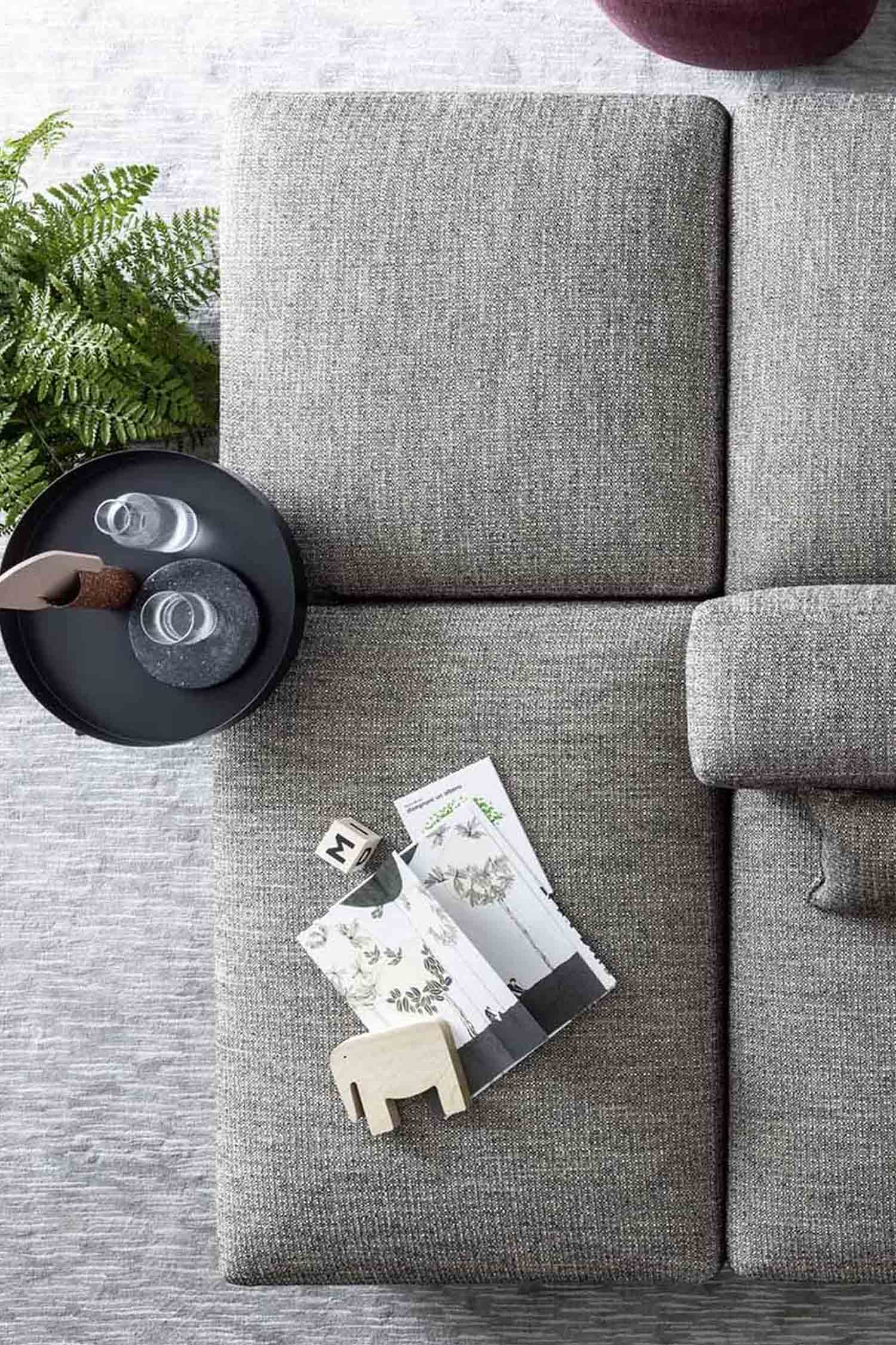 An overhead shot of a light gray modular sofa. A black round tray with two glasses is to the left, and a magazine with a small wooden elephant is on the sofa.