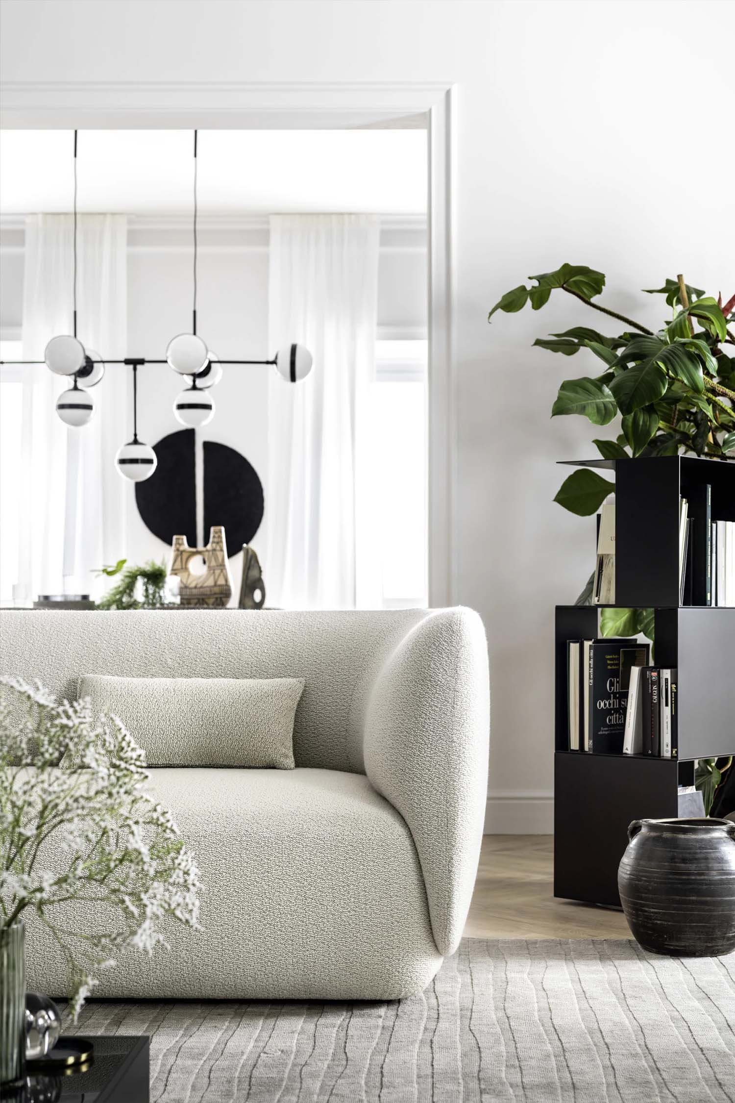 An overhead shot of a blue modular sofa set. The sofa has a curvy, organic shape and is shown with a matching blue ottoman. The arrangement sits on a light floor and a multi-patterned rug. A small white and gold side table with a decorative bowl and a small plant is also visible.