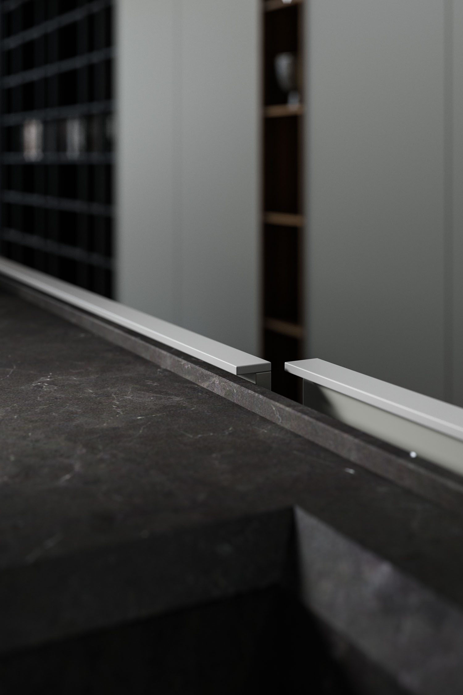 A close-up view of a minimalist kitchen featuring a dark, handleless cabinet with a recessed groove on the top edge that serves as an integrated handle. The cabinet is set against a light-colored stone backsplash.