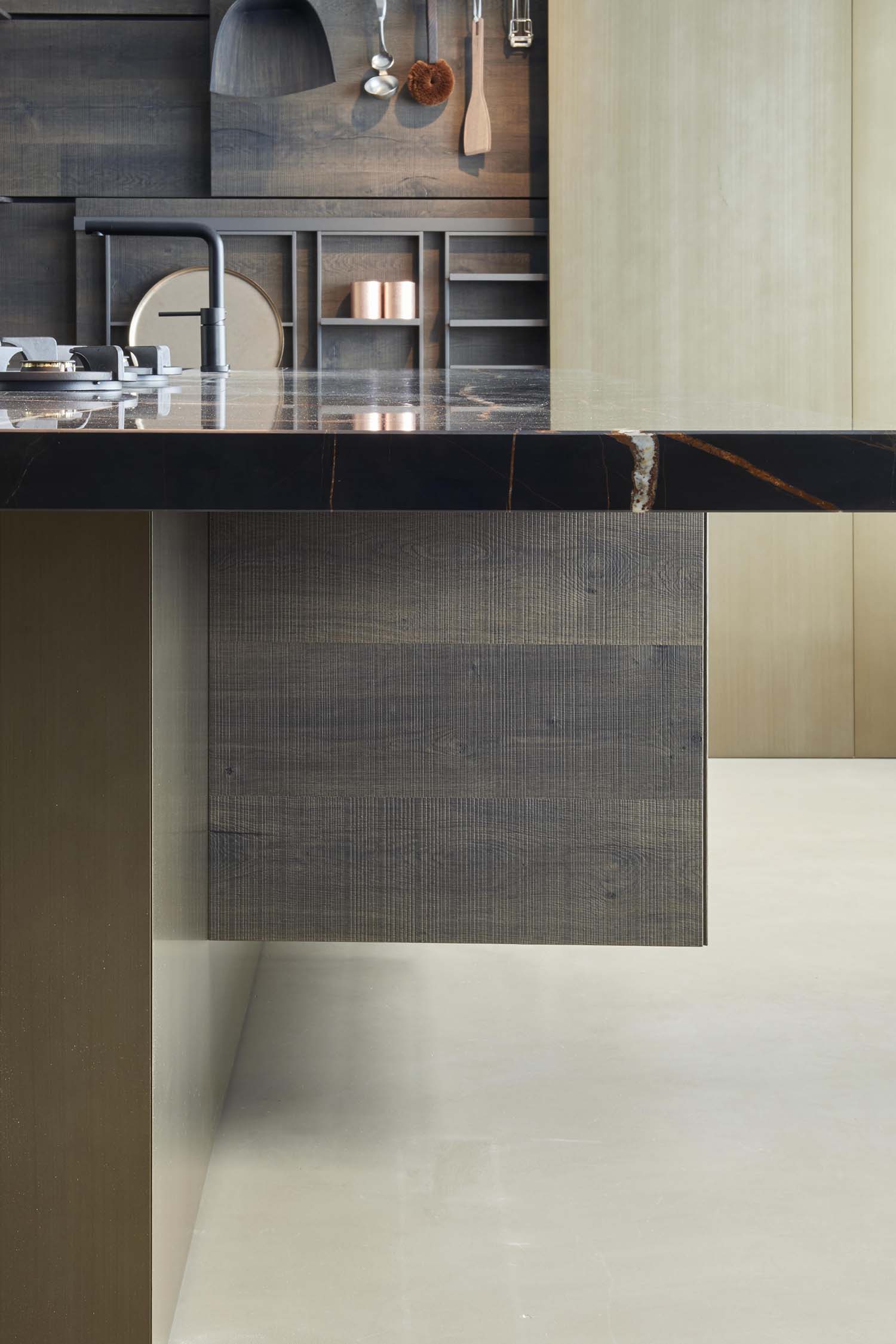 A detailed shot of a kitchen countertop made of light-colored, grey-veined marble. The countertop features a small, integrated wooden cutting board with a modern grater and a round stone bowl.