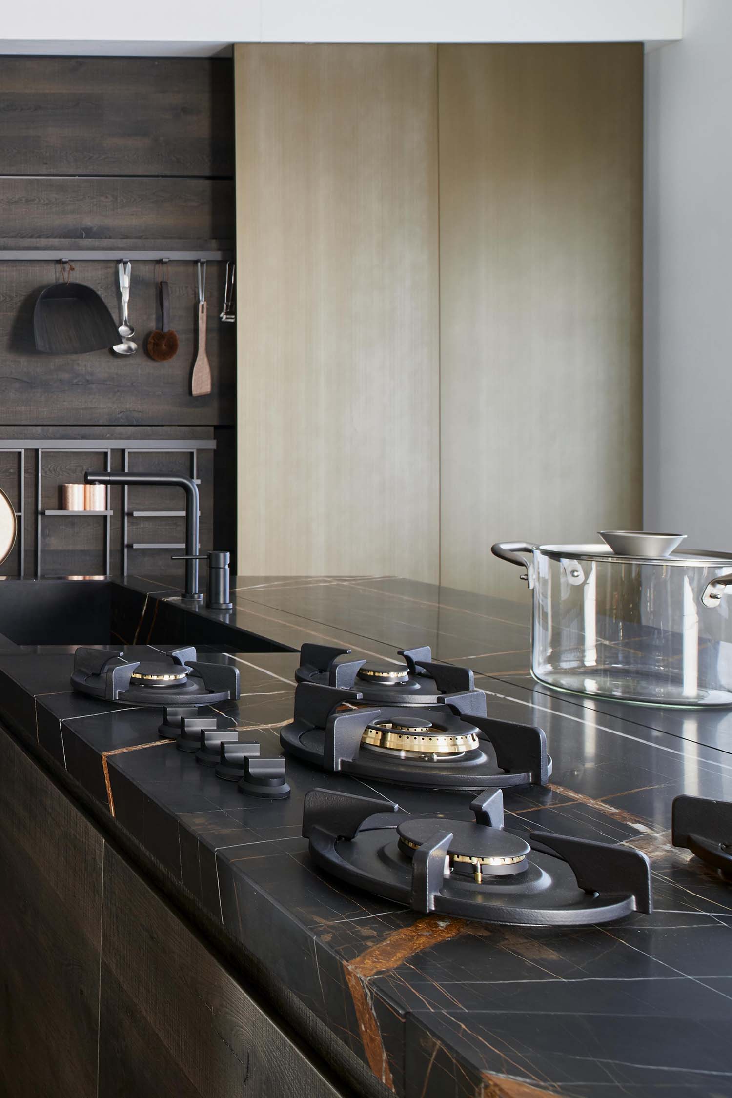 A close-up detail of a minimalist kitchen drawer. The handleless dark wooden drawer is open to reveal a light-colored, wooden interior with a bespoke cutlery organizer and integrated lighting.