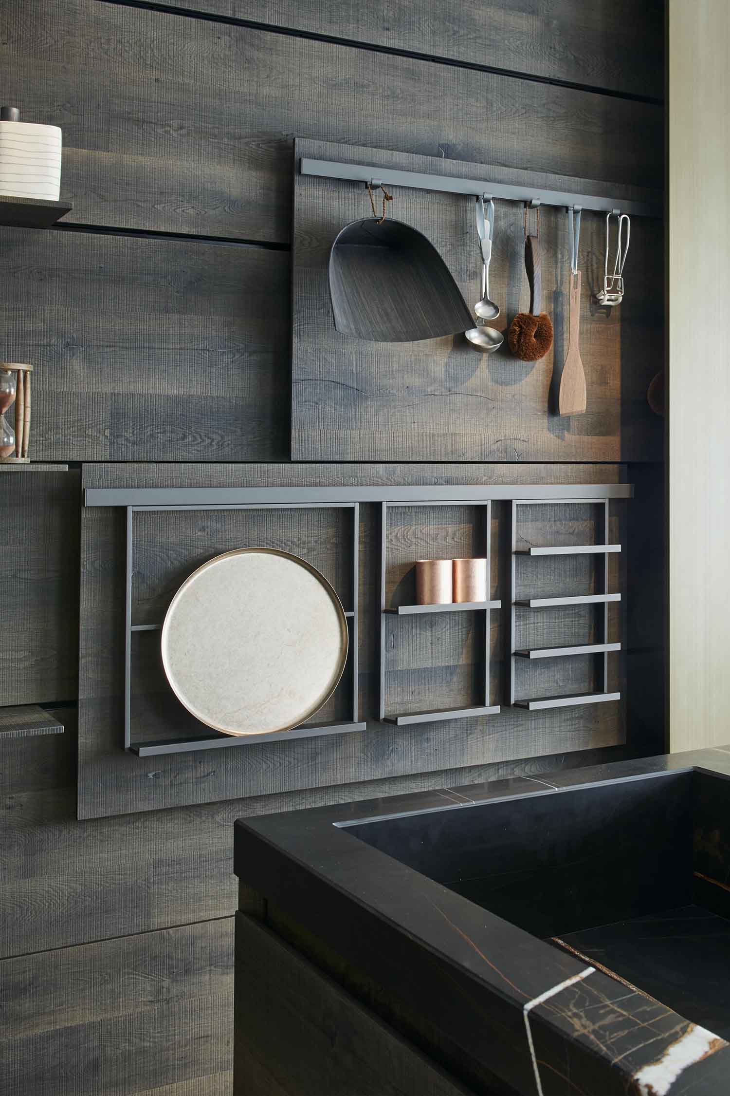 A detail of a minimalist kitchen cabinet with a dark wooden veneer finish. The handleless cabinet door has a thin, recessed groove on the side that serves as a subtle pull.