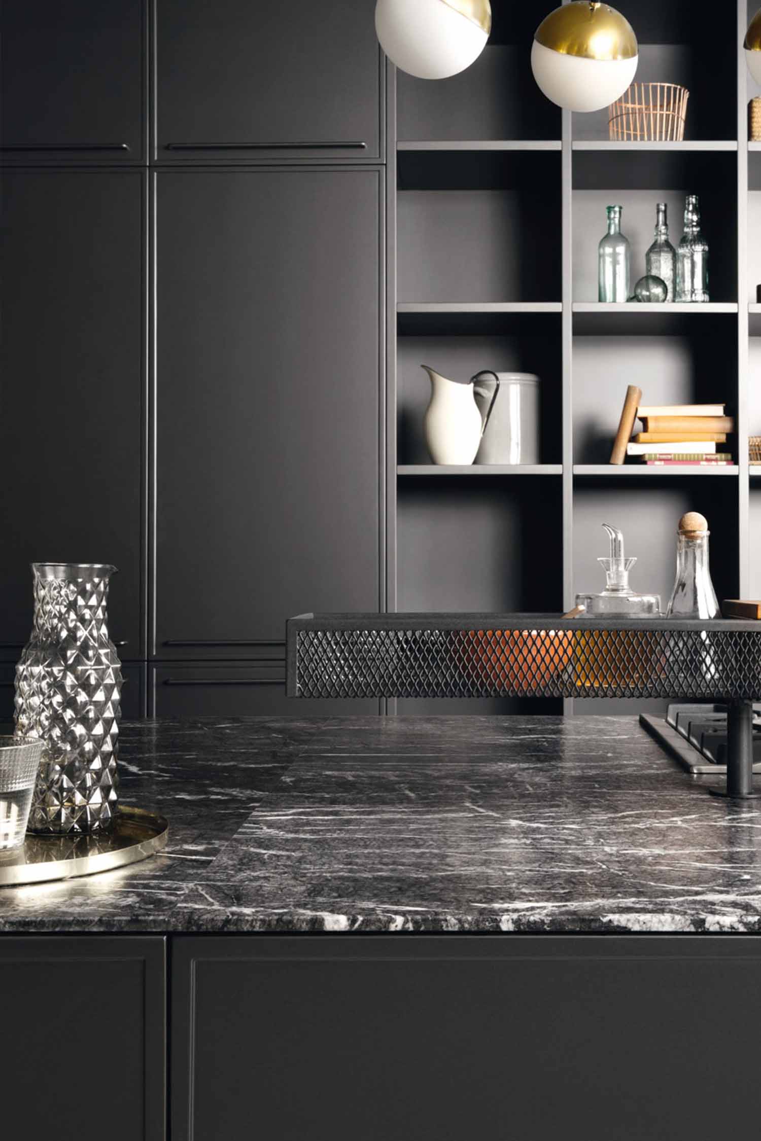 A detail shot of a kitchen's integrated induction hob. The black glass hob is flush-mounted into a light-colored countertop, with a minimalist black vent placed directly behind it.