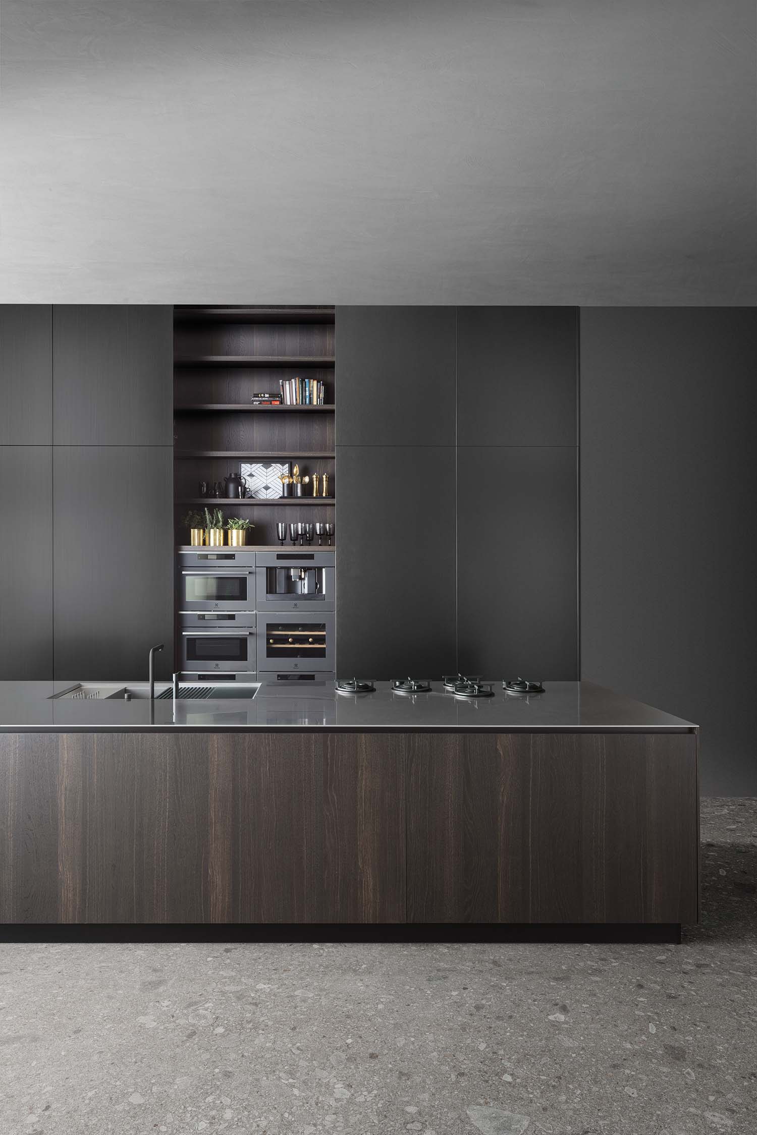 A close-up view of a minimalist kitchen island with a dark wood veneer base and a stainless steel countertop and integrated sink. A sleek, cylindrical faucet is mounted on the counter.