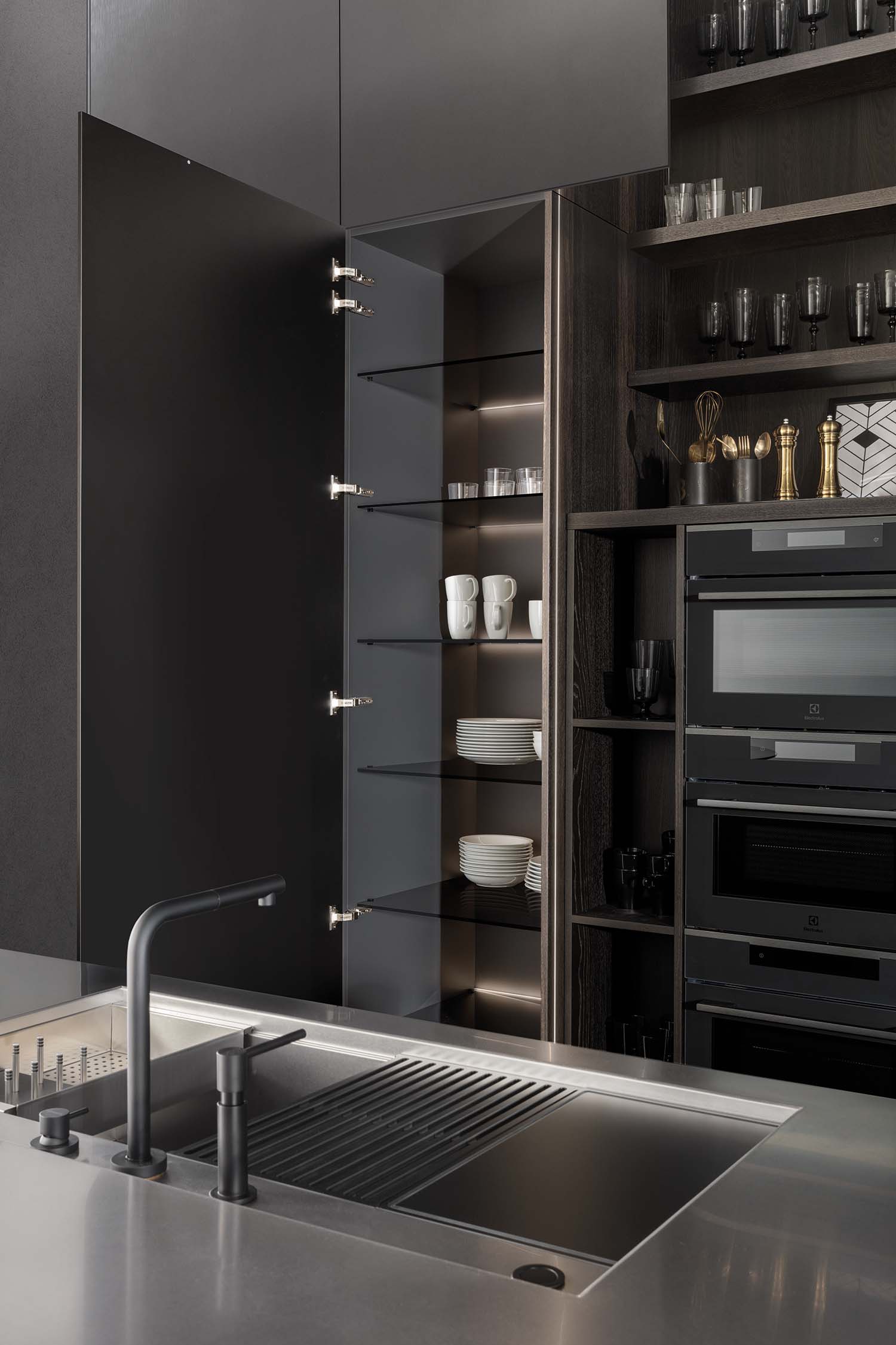 A close-up of an open kitchen drawer revealing a bespoke, dark wooden interior with a pull-out cutting board and a tray with a knife block. The design showcases hidden functionality and efficient use of space.