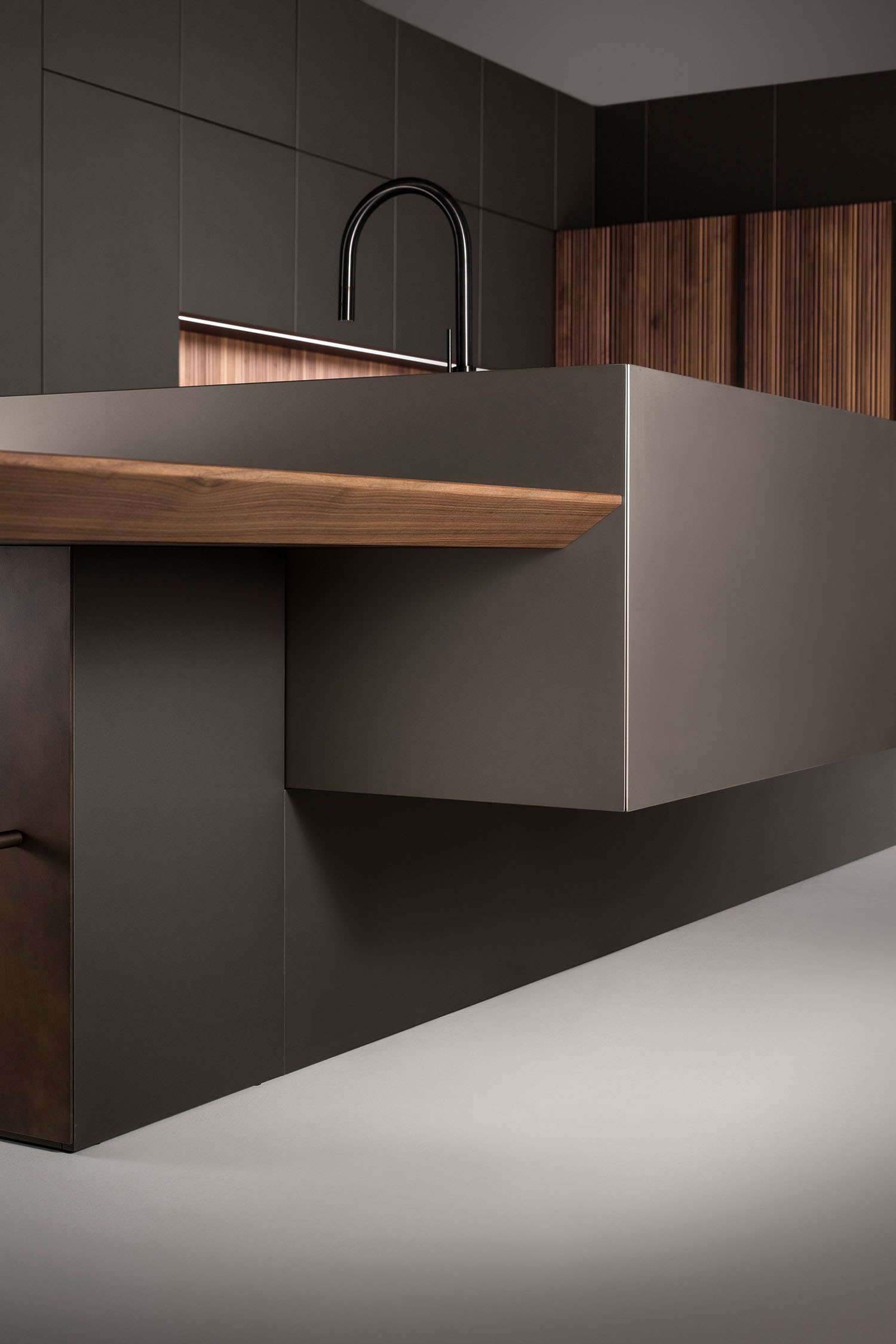 A close-up detail shot of a kitchen's wall-mounted, high-end stripped walnut oak veneer cabinetry. The wood grain is prominent, and a thin, horizontal metal accent strip is visible at the bottom of the cabinet.