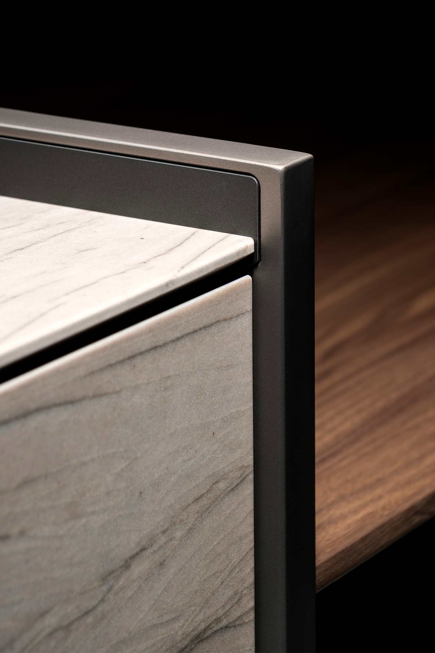 A close-up view of a minimalist, handleless cabinet with a vertical recessed groove on the door, designed to be used as a handle. The cabinet has a dark, matte finish.