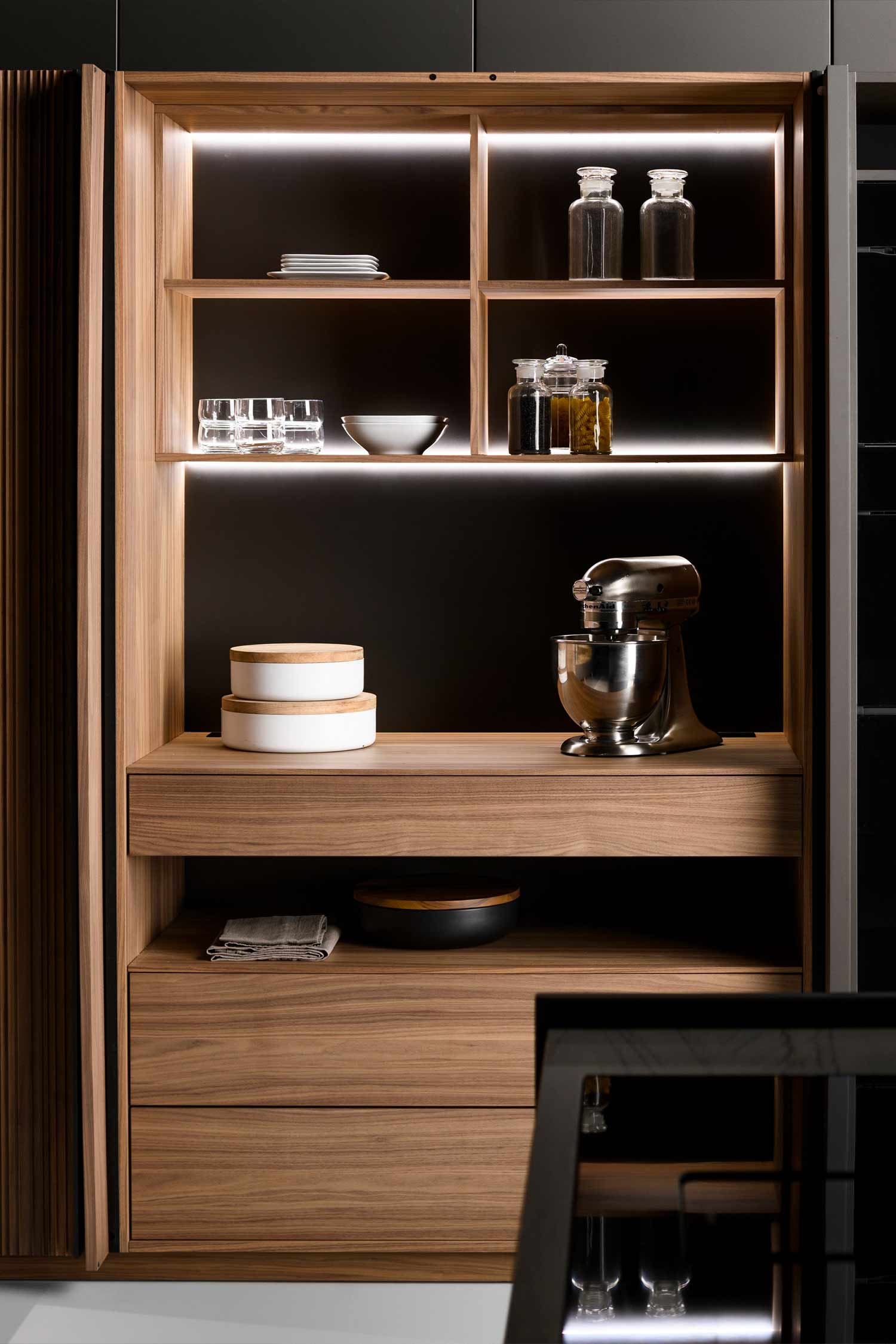 A high-angle, close-up shot of a minimalist kitchen island's countertop, showing a section where the light stone meets a dark, integrated sink. The sink has a modern, rectangular design and a subtle overflow drain.