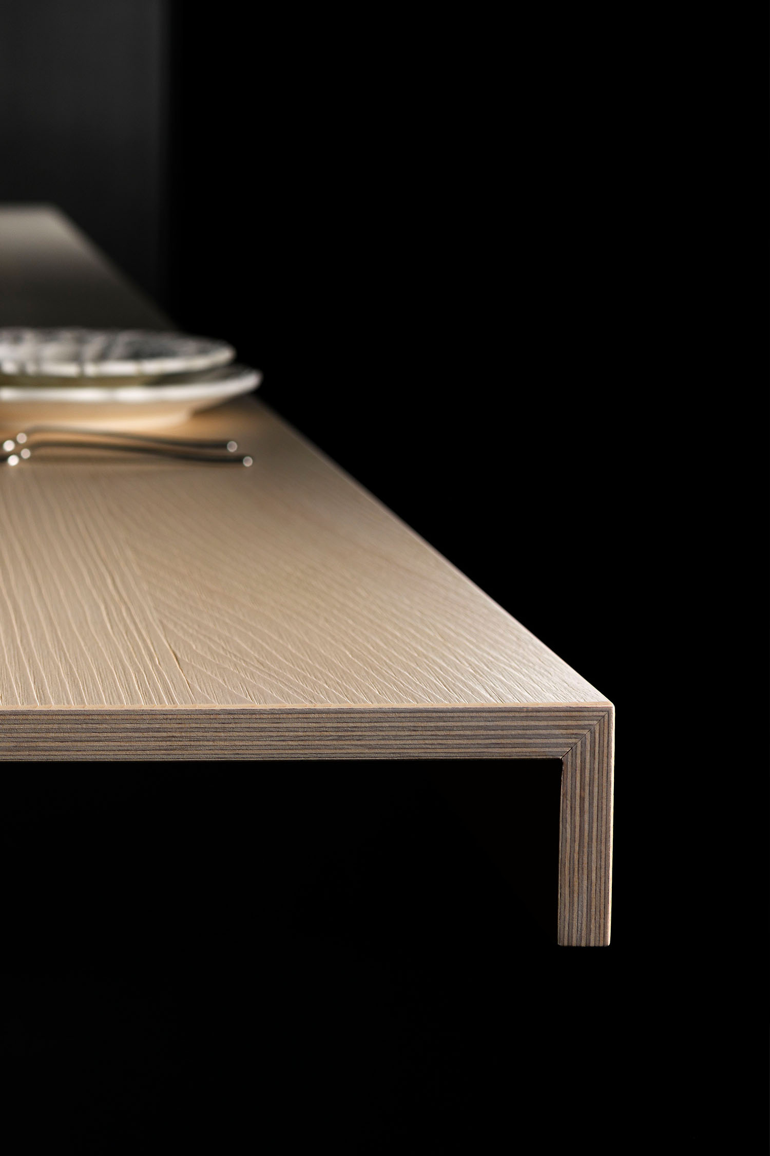 A close-up, low-angle shot of a luxury kitchen's integrated hob and a raised wooden cutting board. The hob is a sleek, black glass surface, and the wood grain on the cutting board is visible.
