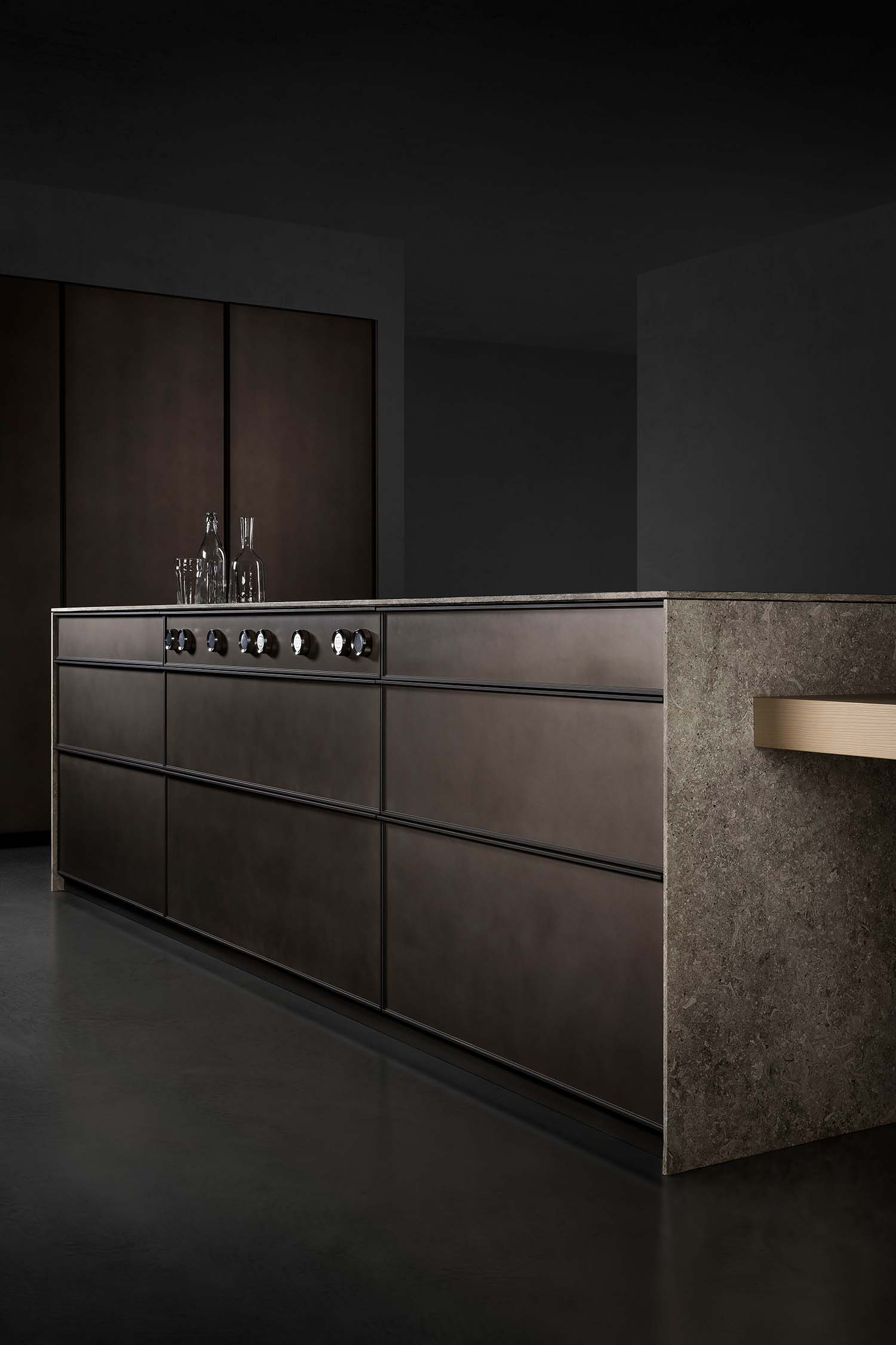 A close-up view of a minimalist kitchen sink. The sink is an integrated white basin with a sleek, black pull-out faucet. The countertop is a light, stone-like material.