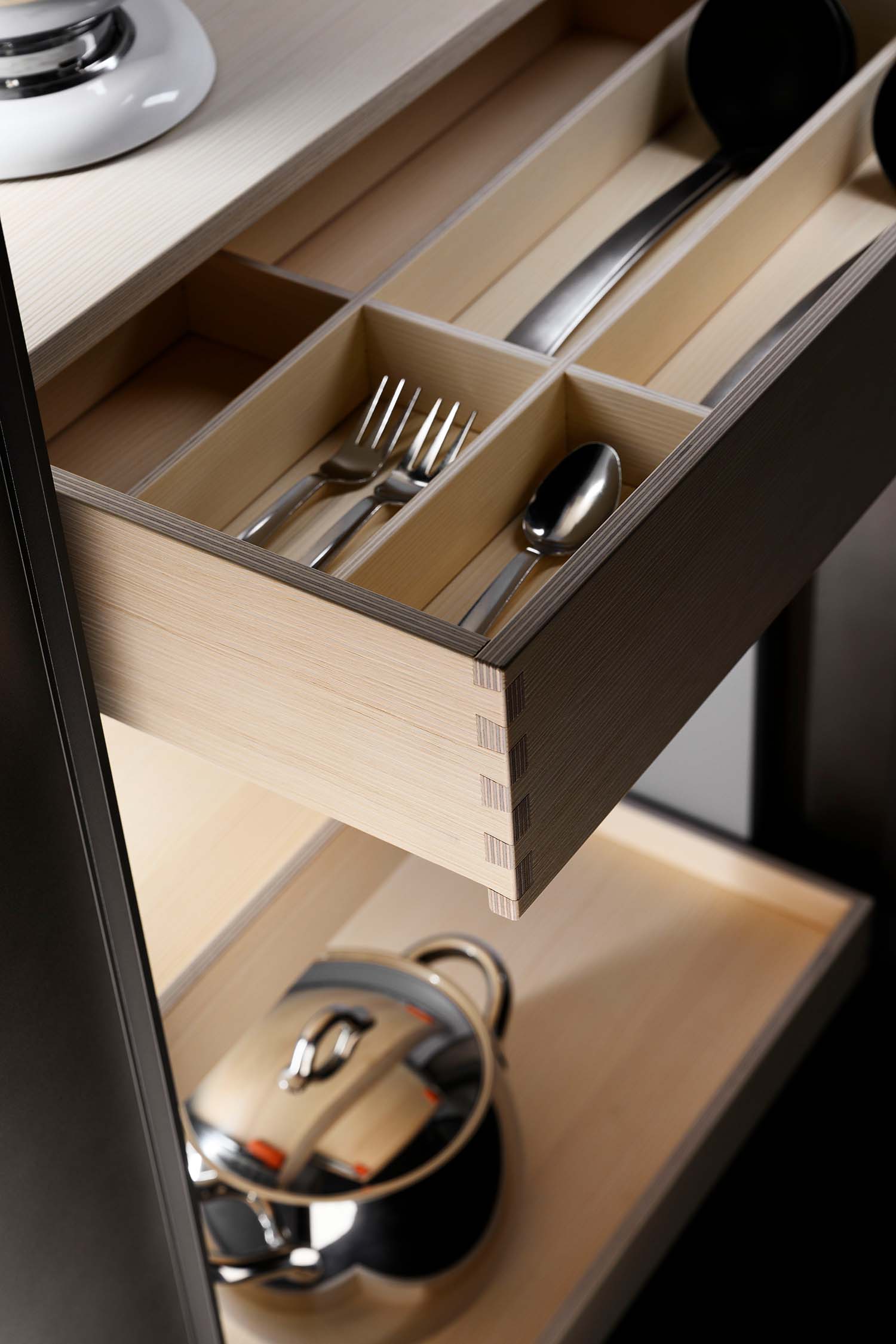 A detail shot of an open kitchen drawer revealing a bespoke wooden divider system. The dividers create compartments for organizing various kitchen utensils and accessories.