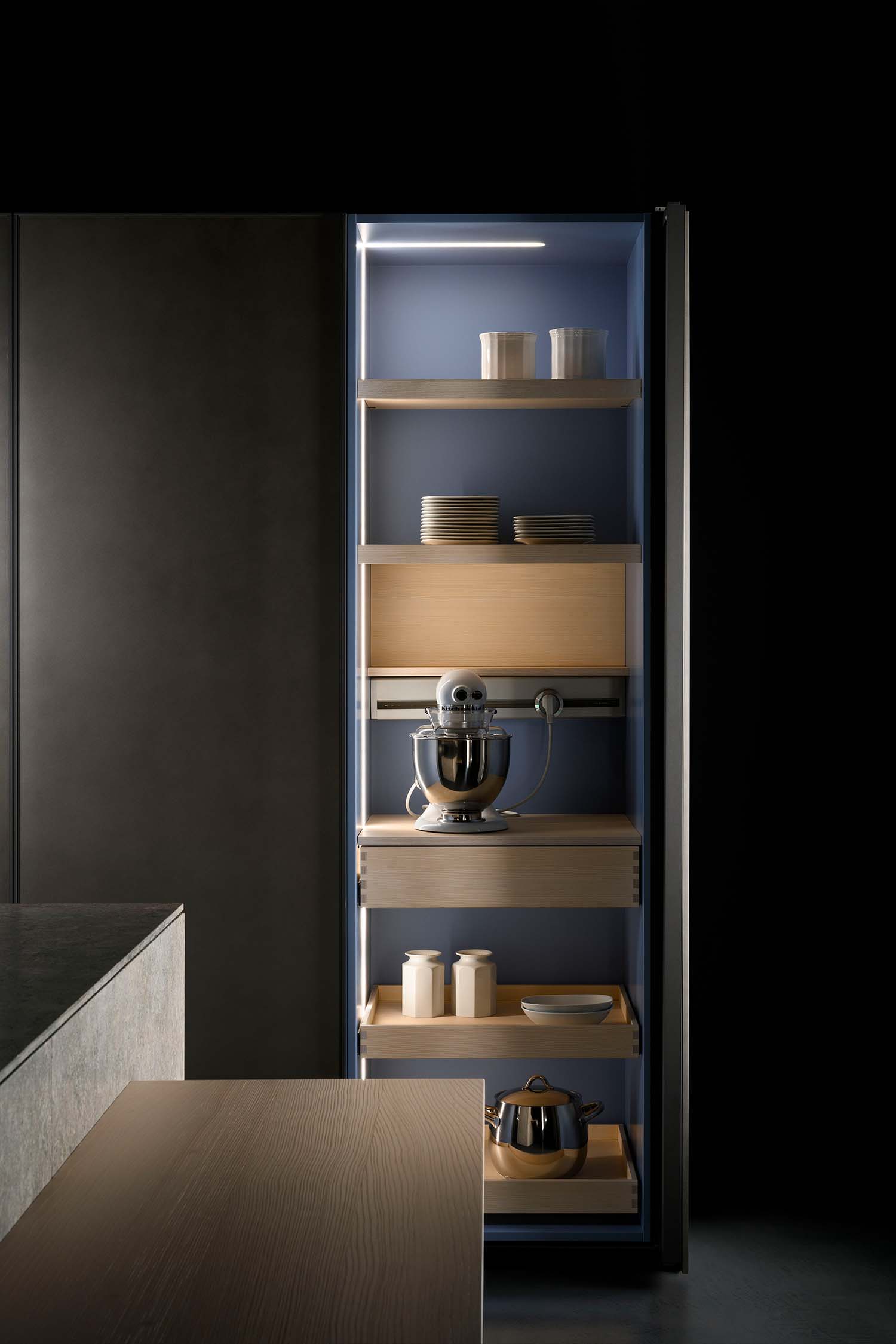 A detail view of a modern kitchen wall with a row of integrated lighting. The light strips are recessed into the wall at the junction of the back wall and the countertop, providing functional task lighting.