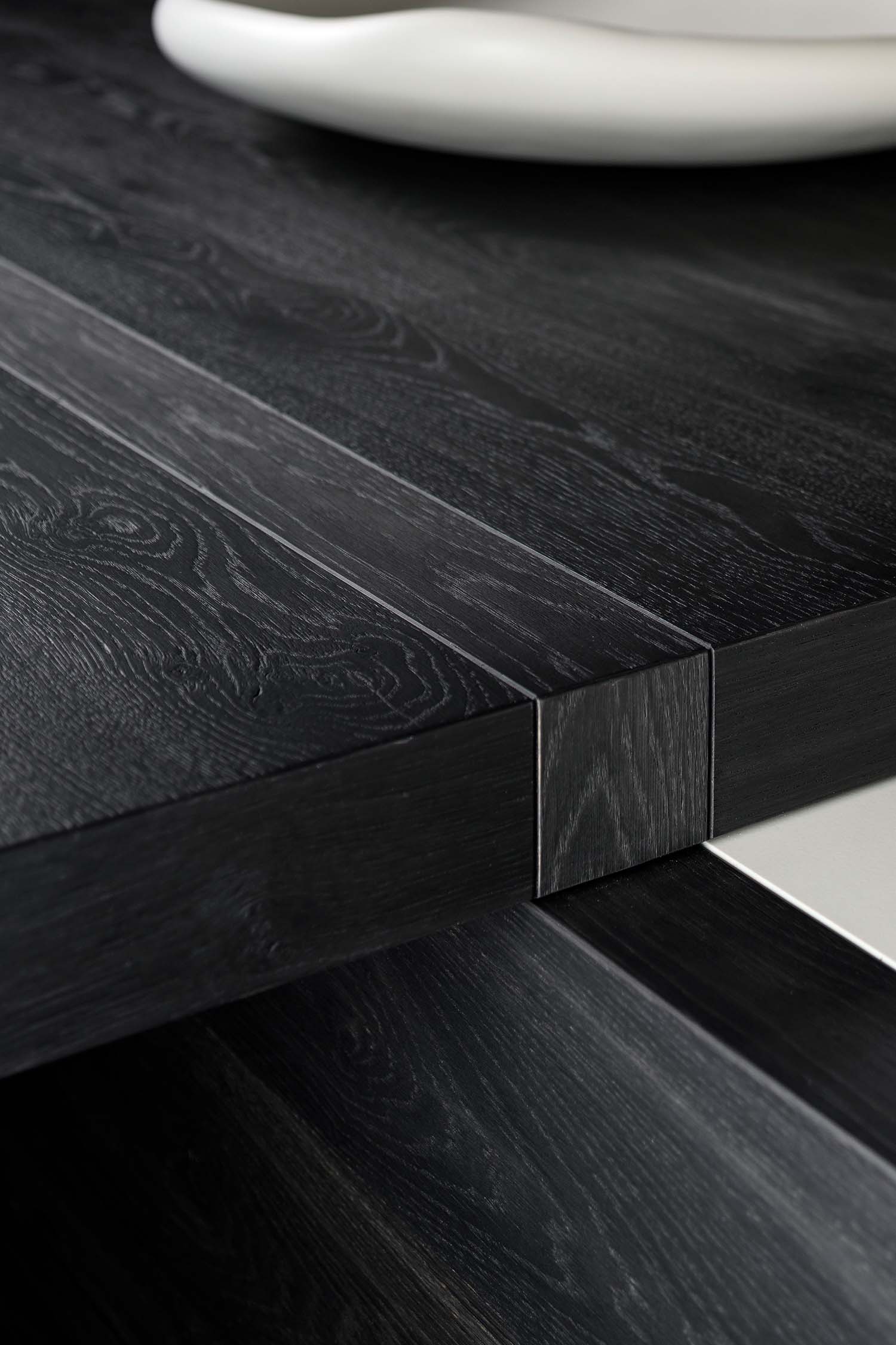 A close-up of a contemporary, built-in kitchen sink. The sink is made of a white material with a subtle marble pattern, and it has a sleek, matte black faucet. The dark wood paneling of the backsplash is visible behind the sink.