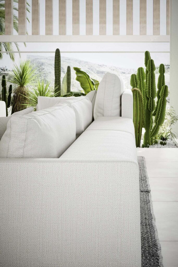 A close-up view of a textured, white sectional sofa with a white cushion against a bright window, showcasing a lush outdoor view with cacti and other desert plants.