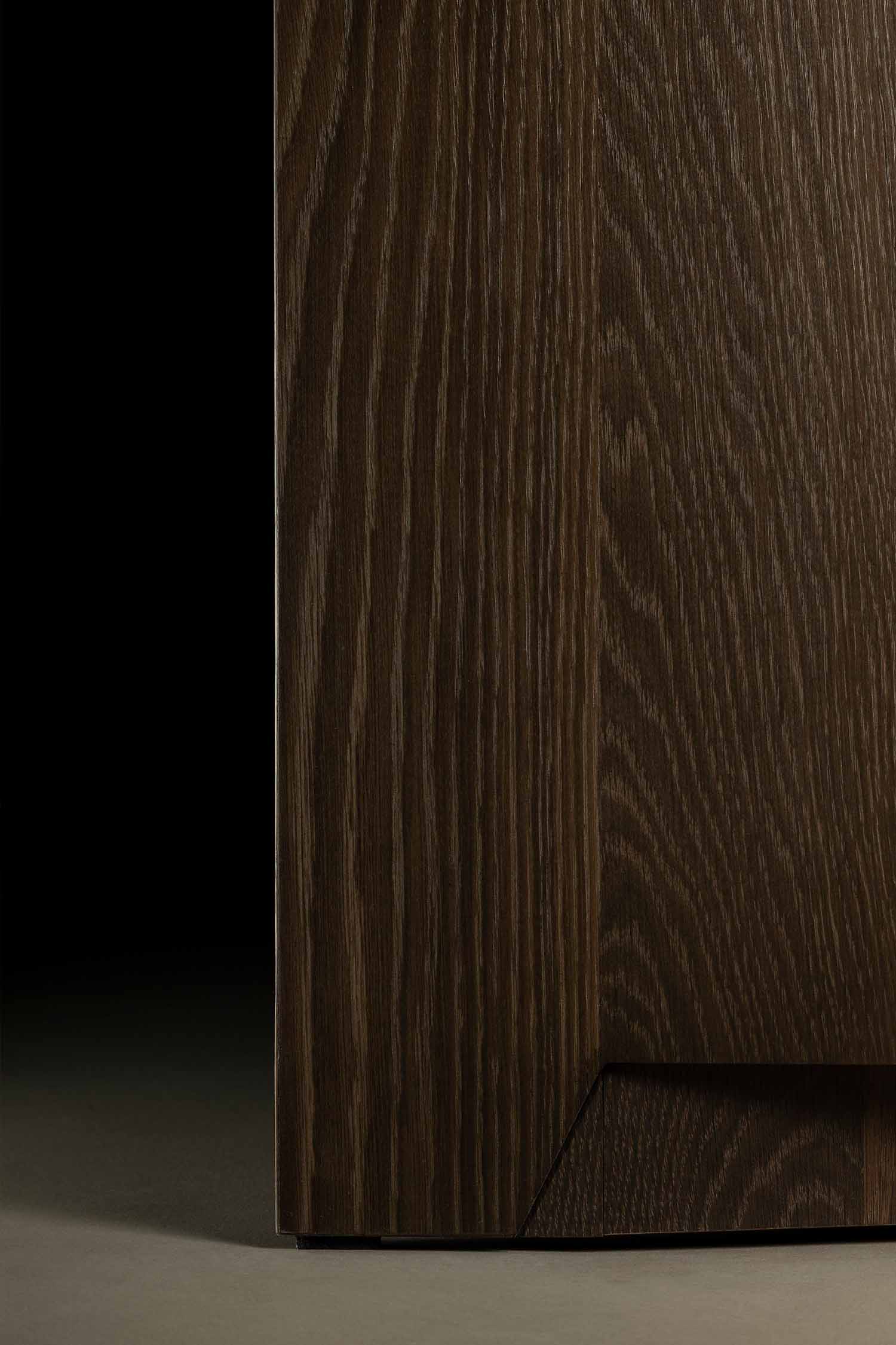 A detailed, close-up image of a dark wood veneer cabinet with a visible grain texture. The cabinet has a unique, diagonal cut at the base that acts as a handle.