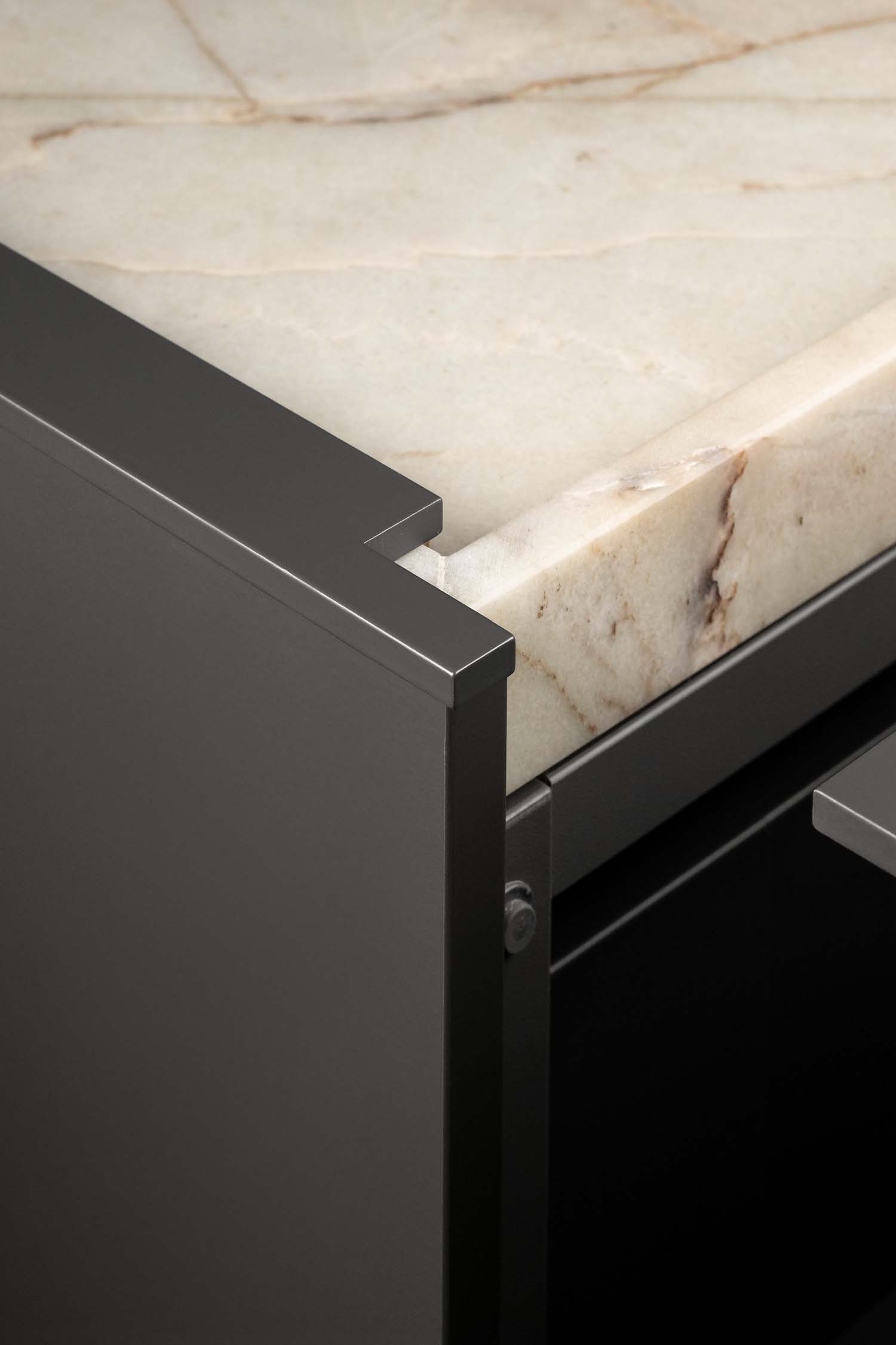 A close-up, low-angle shot showing the joint where the marble countertop meets a dark, contemporary metal cabinet frame. A screw head is visible on the metal leg.