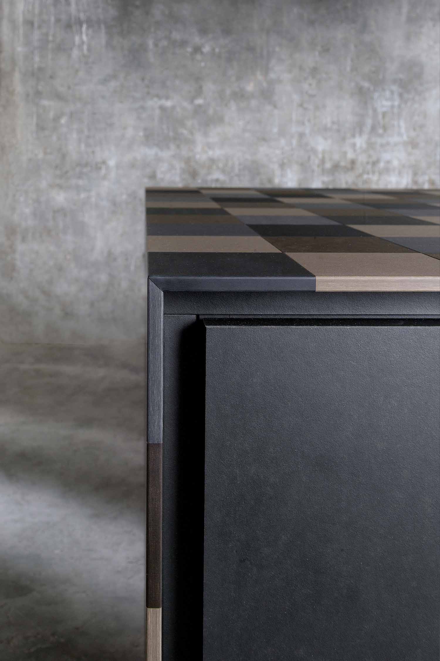 A close-up of a dark, matte-finish kitchen cabinet, highlighting the subtle, horizontal wood grain texture and a thin, horizontal metal handle recessed at the top.