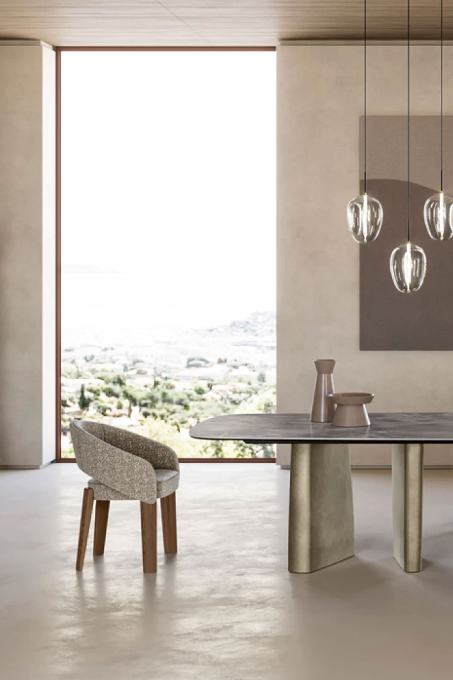 A vertical shot of a contemporary dining set next to a large window overlooking a cityscape and sea view. The foreground features a portion of a dark grey marble-top table supported by two gold-toned pedestal bases. A single modern chair with textured beige upholstery and dark wooden legs is positioned beside the table. Minimalist pottery sits on the tabletop, and clear glass pendant lights hang above.