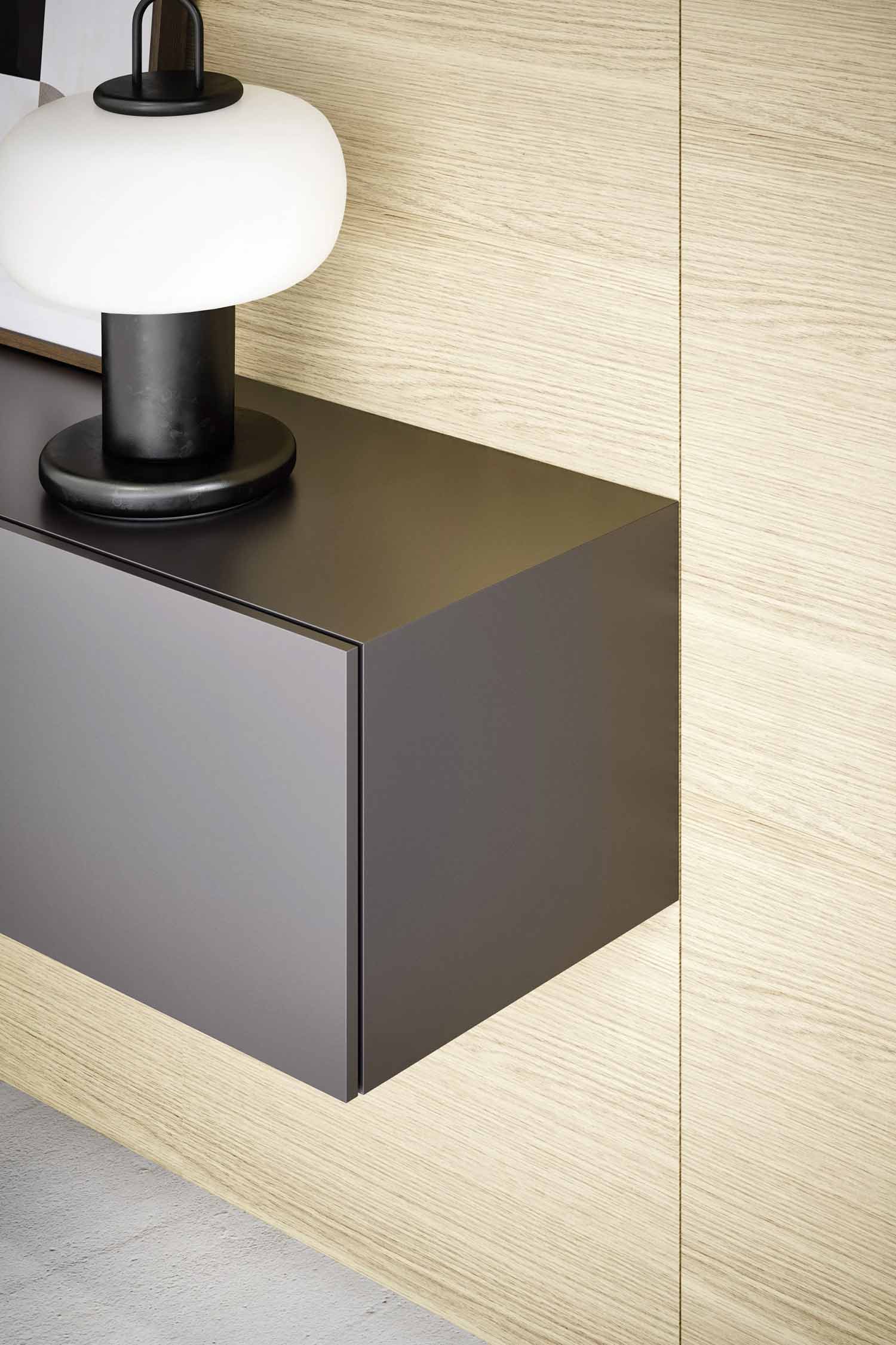 A close-up shot of a dark gray floating cabinet with a single drawer, set against a light wood-paneled wall. A modern table lamp with a white globe and a black base is placed on top of the cabinet.