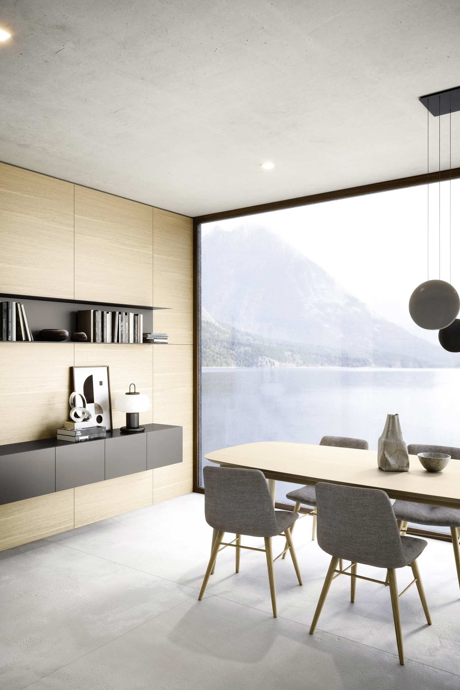 A modern dining room with a custom-built storage unit. The unit is composed of a long dark gray credenza and a floating black shelf, set against a light wood panelled wall. A large window overlooks a beautiful lake and mountains.