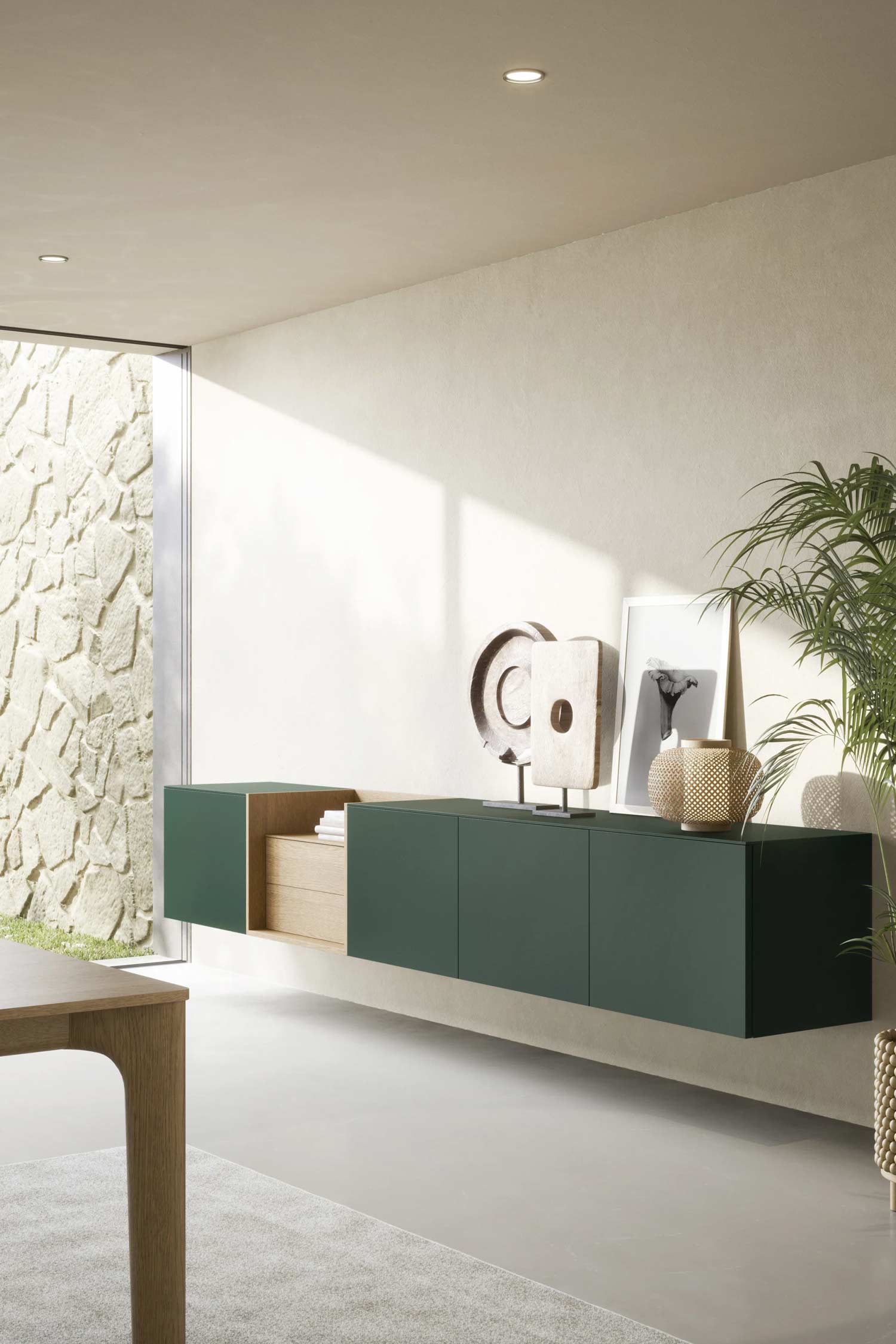 A sleek, modern credenza with a dark gray matte finish and a white marble top. The credenza has four doors and a single open shelf with two books and a decorative box. The piece is supported by thin, gold-colored legs. On top of the credenza, a modern black desk lamp with a brass base, a framed portrait of a woman, and a geometric sculpture are placed. A simple round mirror with a thin brass frame hangs on the white wall above the credenza.