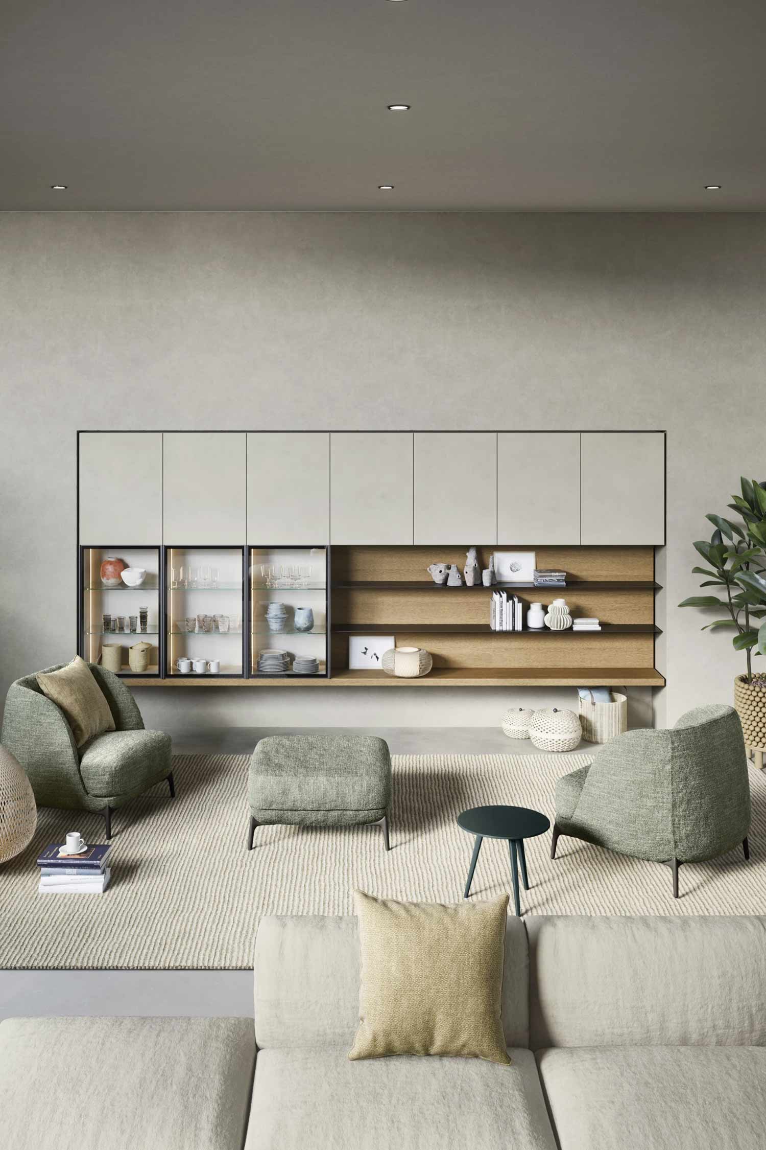 A modern living room with a low-profile, two-tone storage unit against a light gray wall. The unit features light-colored upper cabinets, open wood shelving below, and two glass display cases on the left. Two light green armchairs with an ottoman sit on a large, textured rug facing the storage unit.