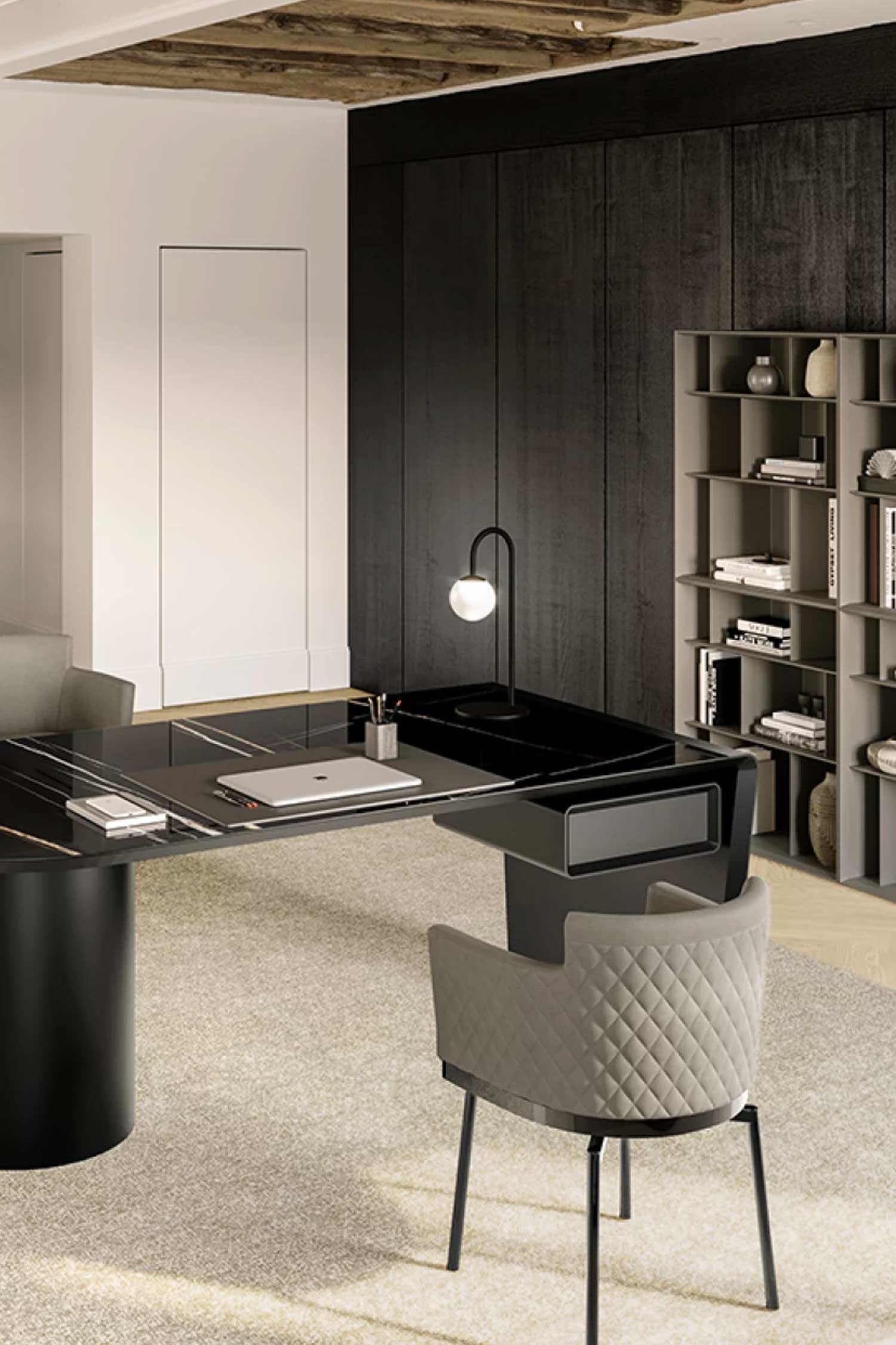 Detailed view of the black marble-effect Cilindro desk corner in a modern office with dark wood paneling and a tall, modular bookshelf. A gray upholstered, quilted chair is pulled up to the desk, and a simple globe lamp provides light on the tabletop.