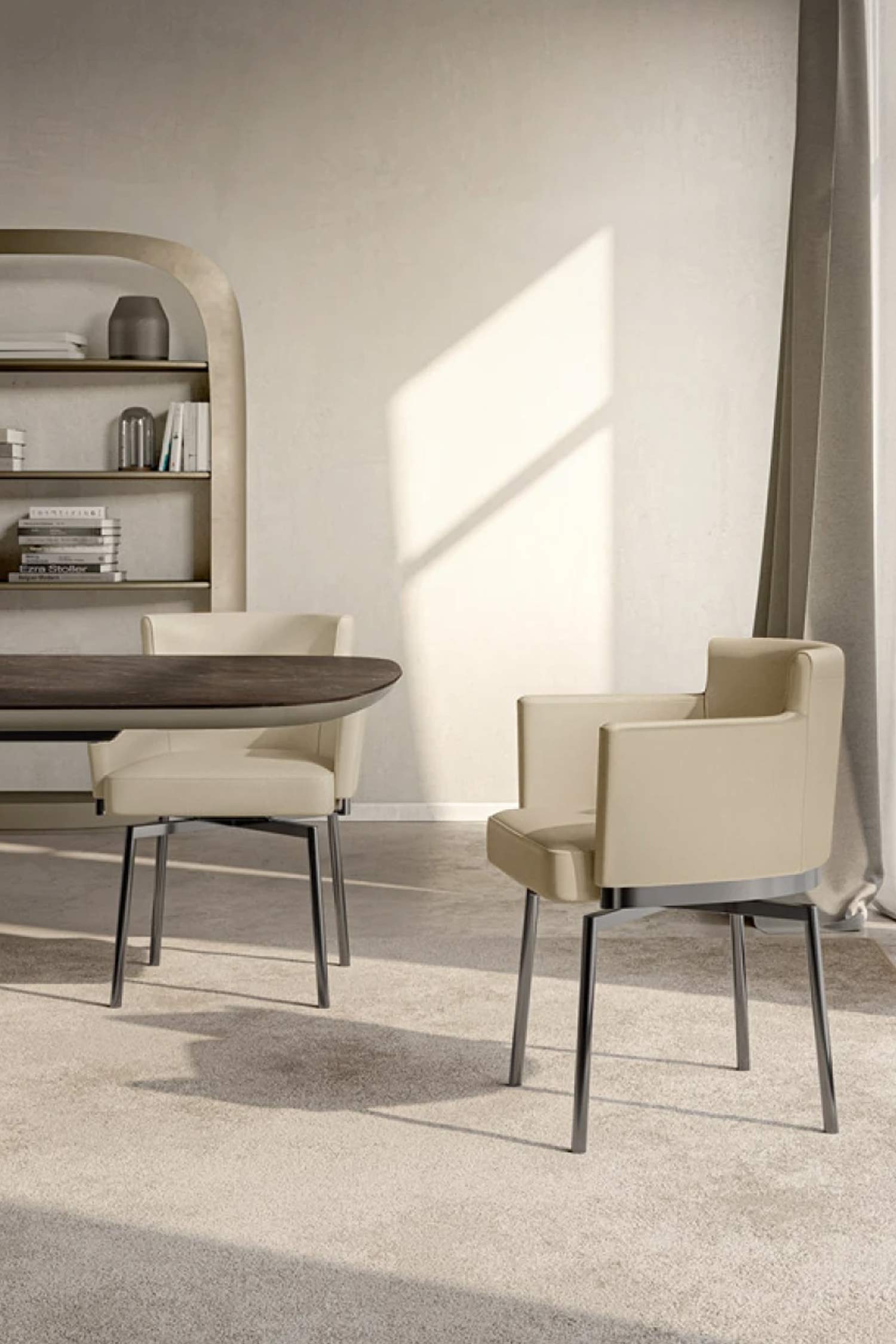 Two cream-colored, contemporary dining chairs with thin metal legs are shown in a modern dining room with a large window and a dark wood table. A curved bookshelf is visible in the background.