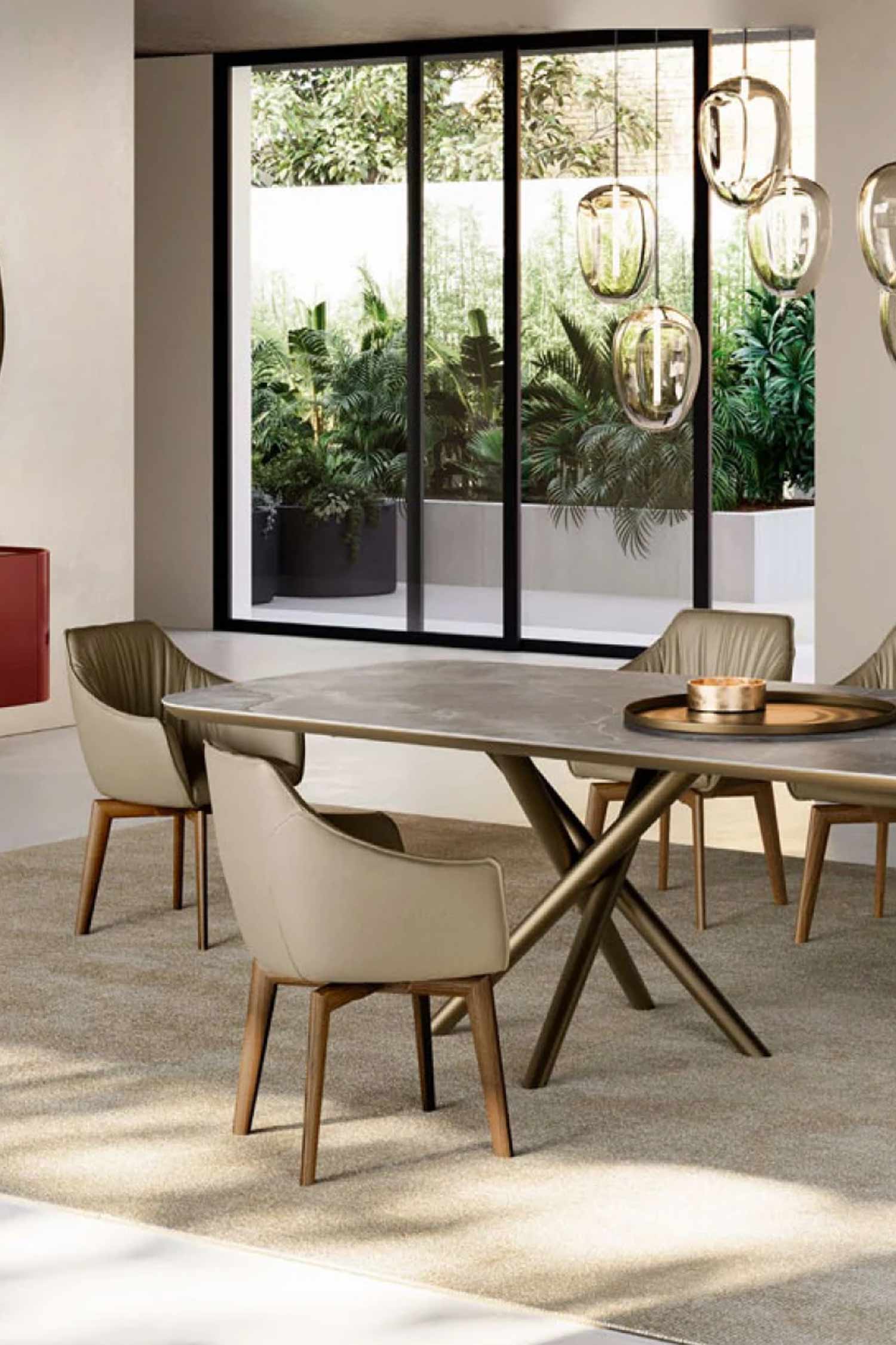 A dining room scene showing a portion of a modern dining table with a marbled top and geometric base. Two chairs with cream upholstery and wooden legs are visible, with a large window and green plants in the background