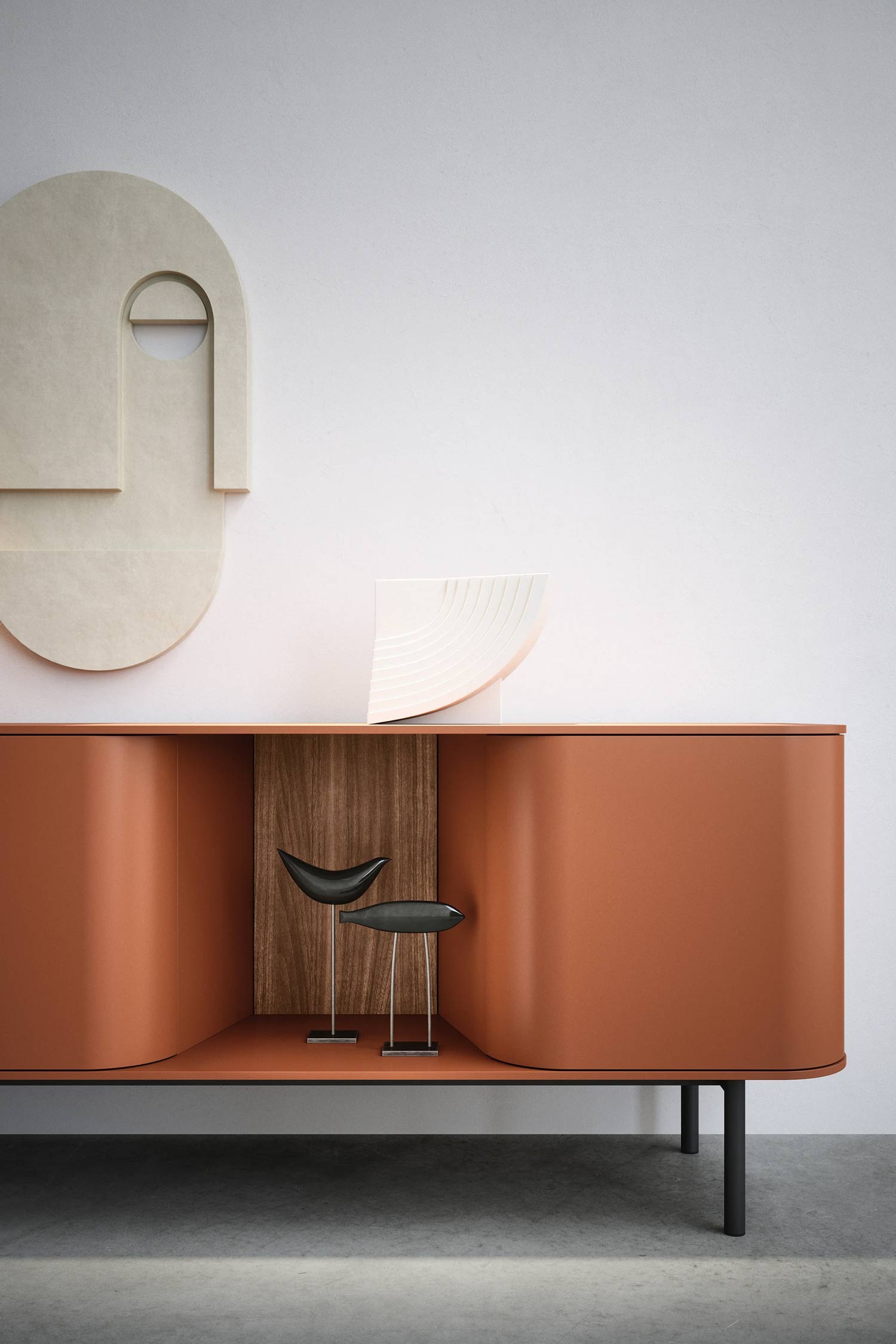 A modern, terracotta-colored sideboard with two curved open compartments. The left compartment features two black bird-shaped figurines, while the right compartment has a wooden back panel. On top of the sideboard, a light wood, fan-shaped sculpture is displayed. Above the sideboard, a large, beige, abstract wall decoration in the shape of a face is mounted on a light-colored wall.