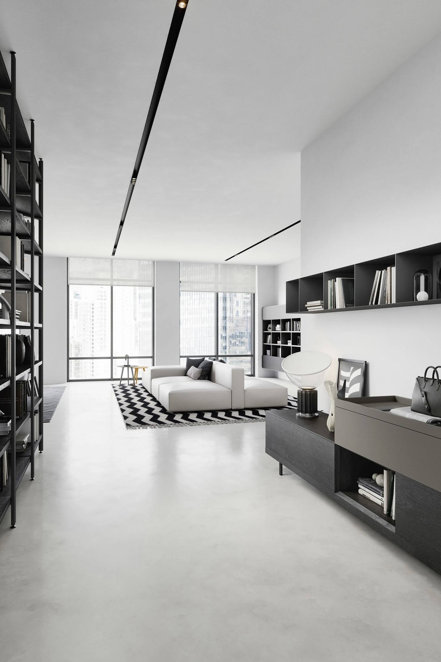 A minimalist living room is shown with a large white sectional sofa and a black and white geometric rug. The room has large windows with a city view and track lighting on the ceiling. On the right, a dark wood console table with a gray storage unit holds books and decor. A tall, black open bookshelf stands on the left.