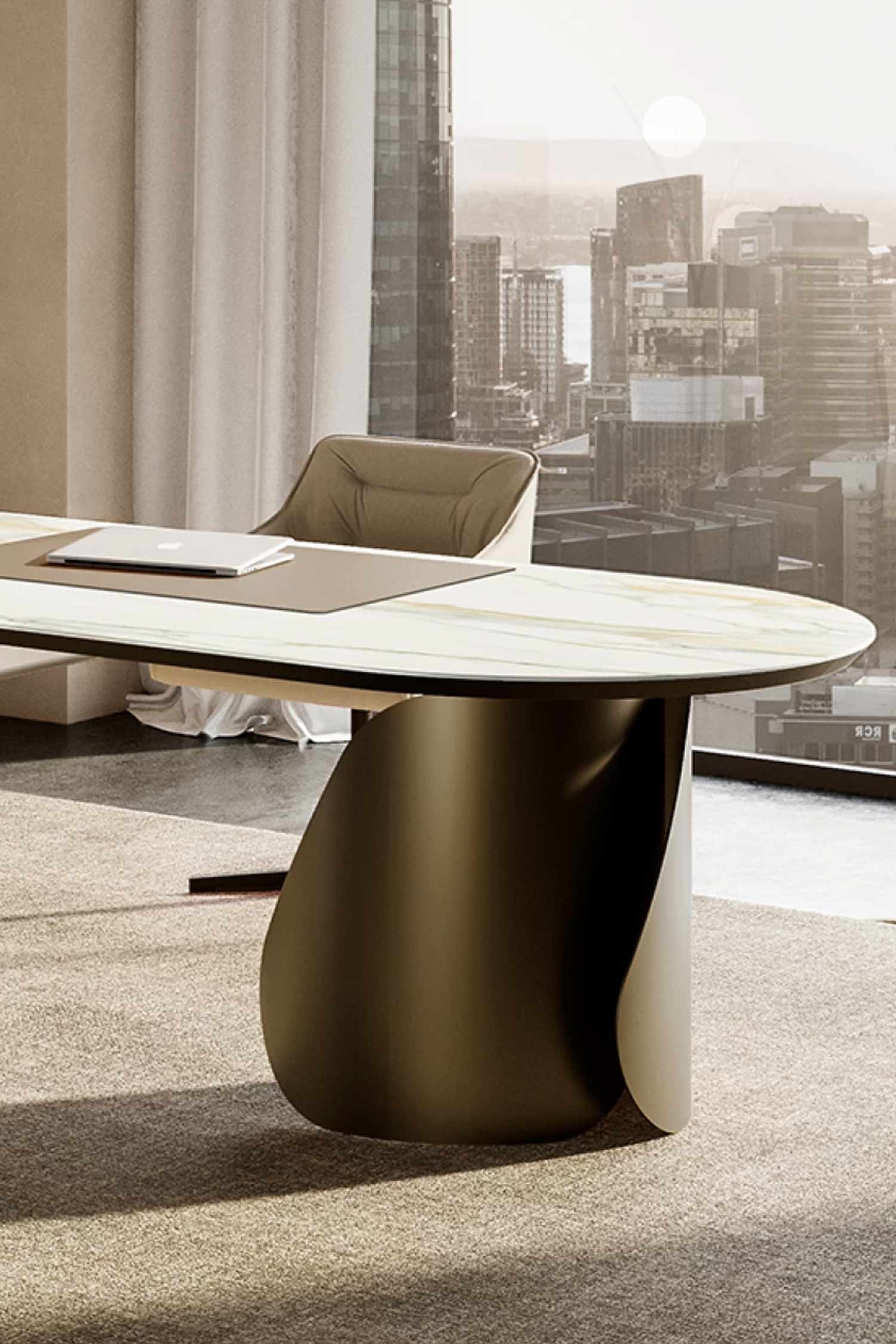 A close-up detail of a luxury office desk with a white marble oval top and a bronze-toned, sculptural curved base. A laptop and desk pad are on the surface, and a light tan office chair is visible behind the desk, set against a large window with a sunlit city skyline view.