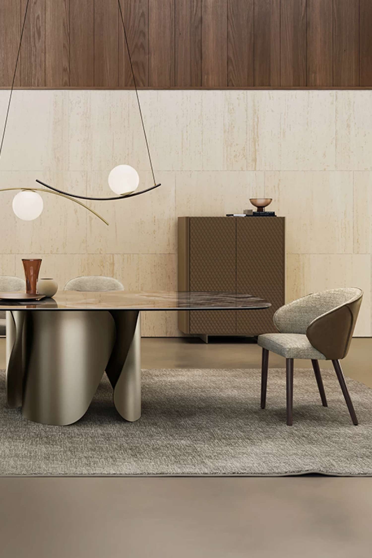 Full view of the Onda dining table with a glossy stone top and bronze-toned metallic base, surrounded by upholstered dining chairs, an overhead modern curved pendant light, and a patterned cabinet in a spacious, light-colored room.