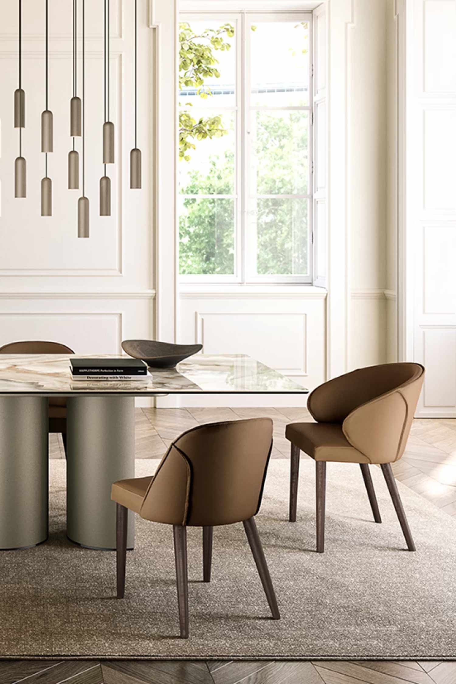 Detail shot of a luxurious dining area showing the taupe cylindrical base of the table, two curved brown leather dining chairs with dark wood legs, and multiple modern pendant lights hanging in the background near a large window.