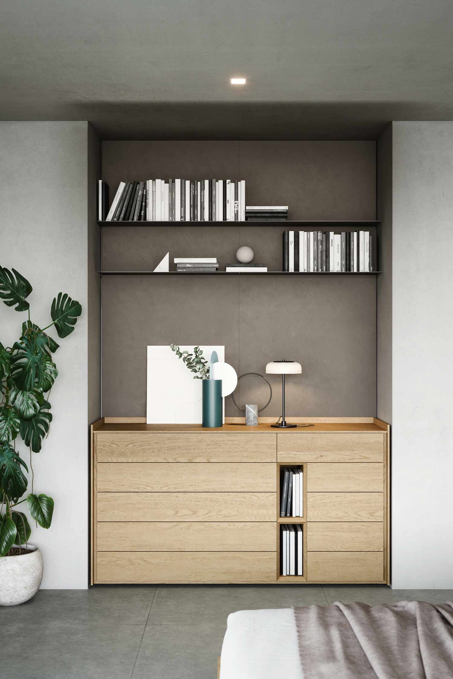 A light wood dresser with five drawers and two tall, narrow, open shelving compartments for books, built into a dark gray niche. The wall unit features two metal shelves filled with books and decorative objects.