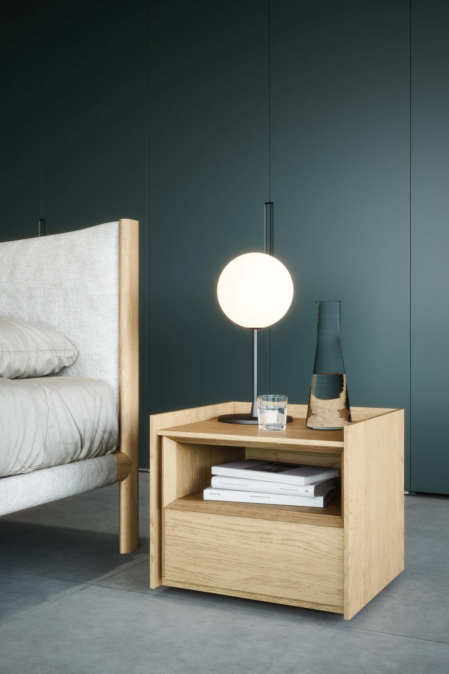 A close-up of a light wood nightstand with one drawer and an open shelf, sitting next to a bed with a light gray upholstered and wood-framed headboard. The nightstand holds a globe-shaped table lamp and a dark glass vase.