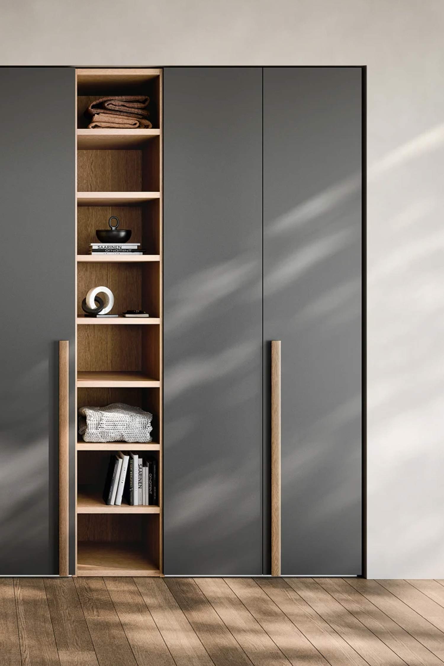A contemporary, dark gray wardrobe with a tall, open-shelving unit in the middle. The shelves are made of light wood and hold folded clothes, books, and decorative items. The hinged wardrobe doors on either side have long, vertical wooden handles.