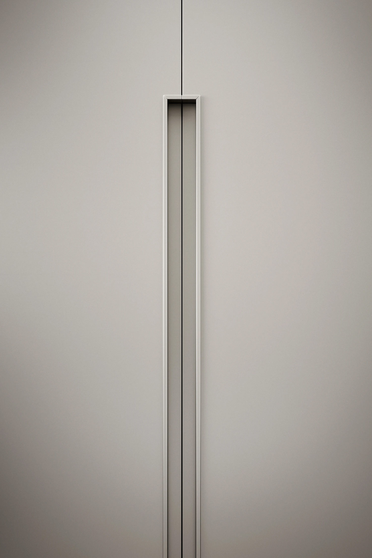 A vertical, close-up view of a minimalist, light gray wardrobe door. The focus is on the long, recessed vertical handle, which is a rectangular, metallic frame that runs from the top to the bottom of the door. The handle has a thin, dark line running down its center, emphasizing the sleek, contemporary design and clean lines of the furniture.