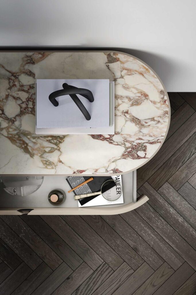Overhead detail shot of a Vesta luxury drawer nightstand with a rectangular, marble top and an open drawer showing internal organization with a magnifying glass and small accessories.