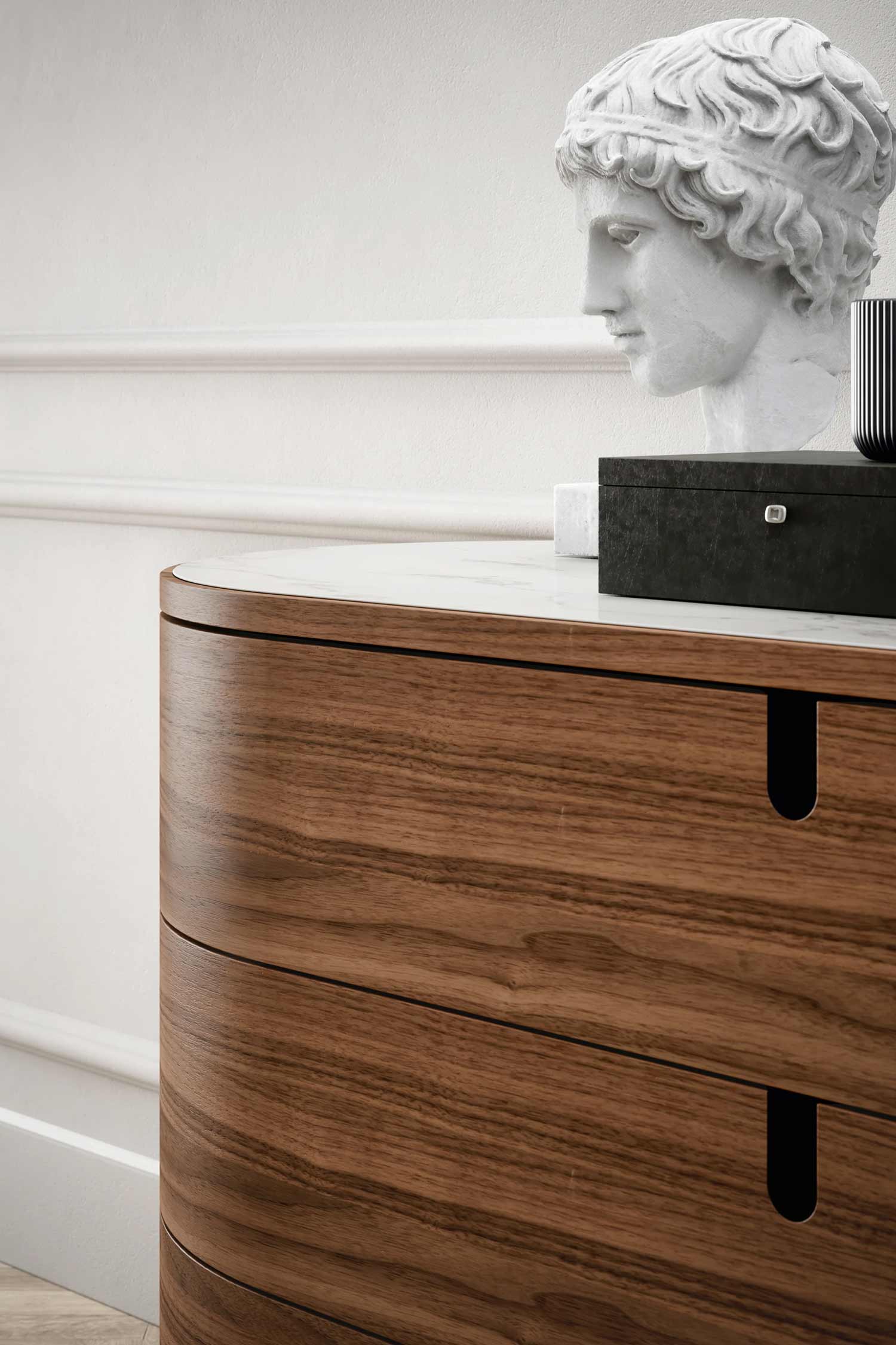 Close-up detail of the curved front of a walnut wood Vesta luxury three-drawer chest, showing the seamless design and marble top, with a classical statue bust decoration.