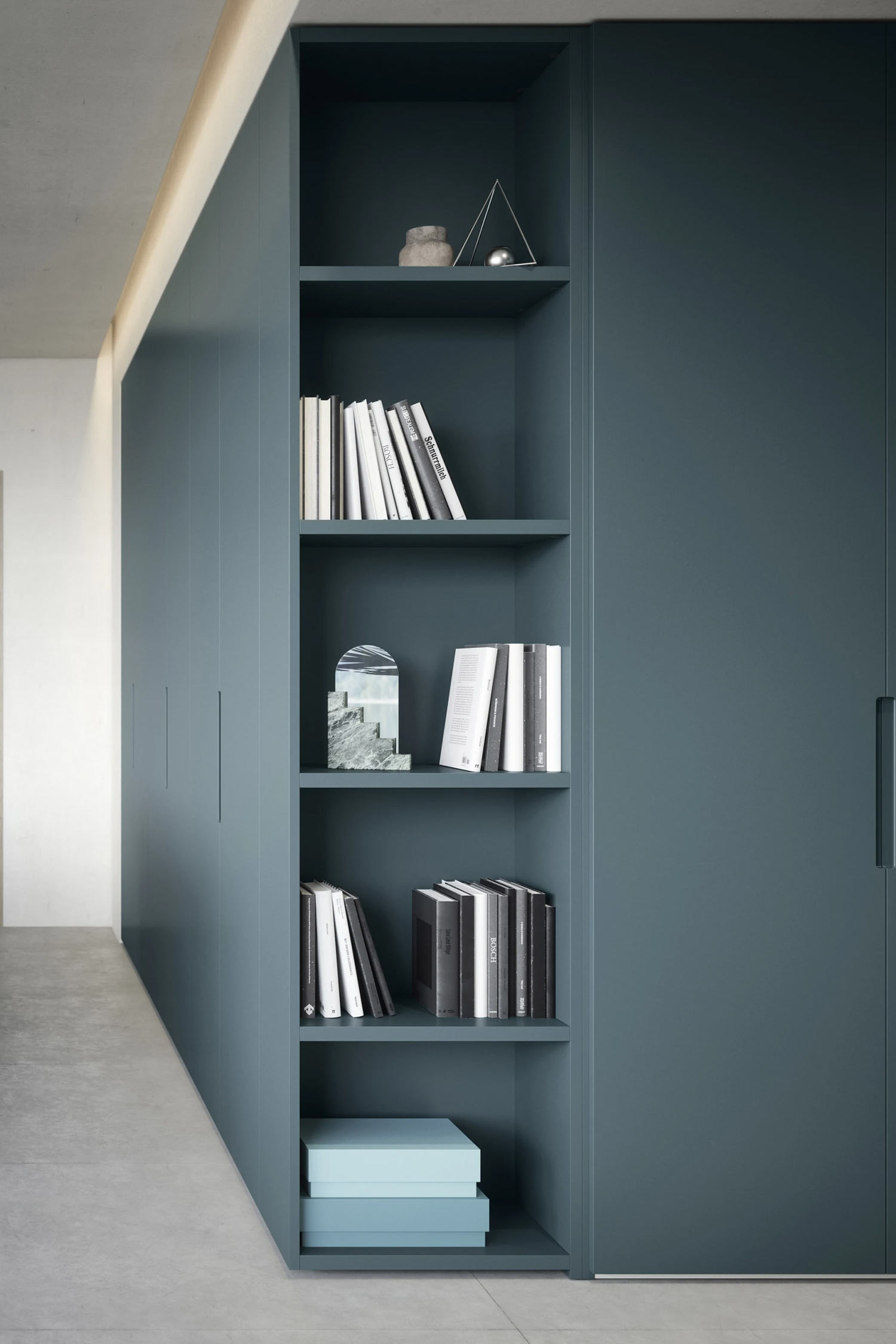 This image shows a close-up of a Vico wardrobe unit in a dark teal or blue-gray color. The unit features an integrated open bookshelf section with several shelves filled with books and decorative objects.