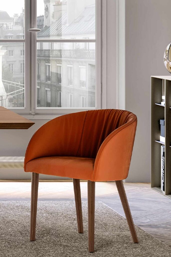 Detail shot of the pleated back and curved shape of an orange velvet Vulcano luxury dining chair in a dining room interior.