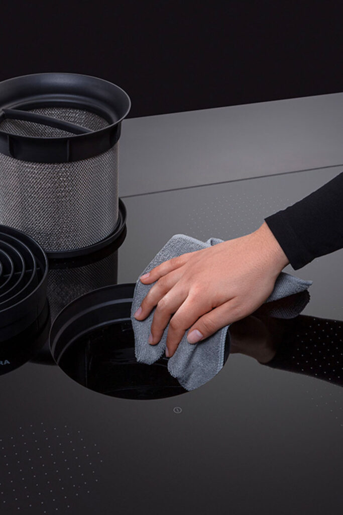 Hand wiping the surface of a BORA Pure S cooktop with the vent removed for cleaning.