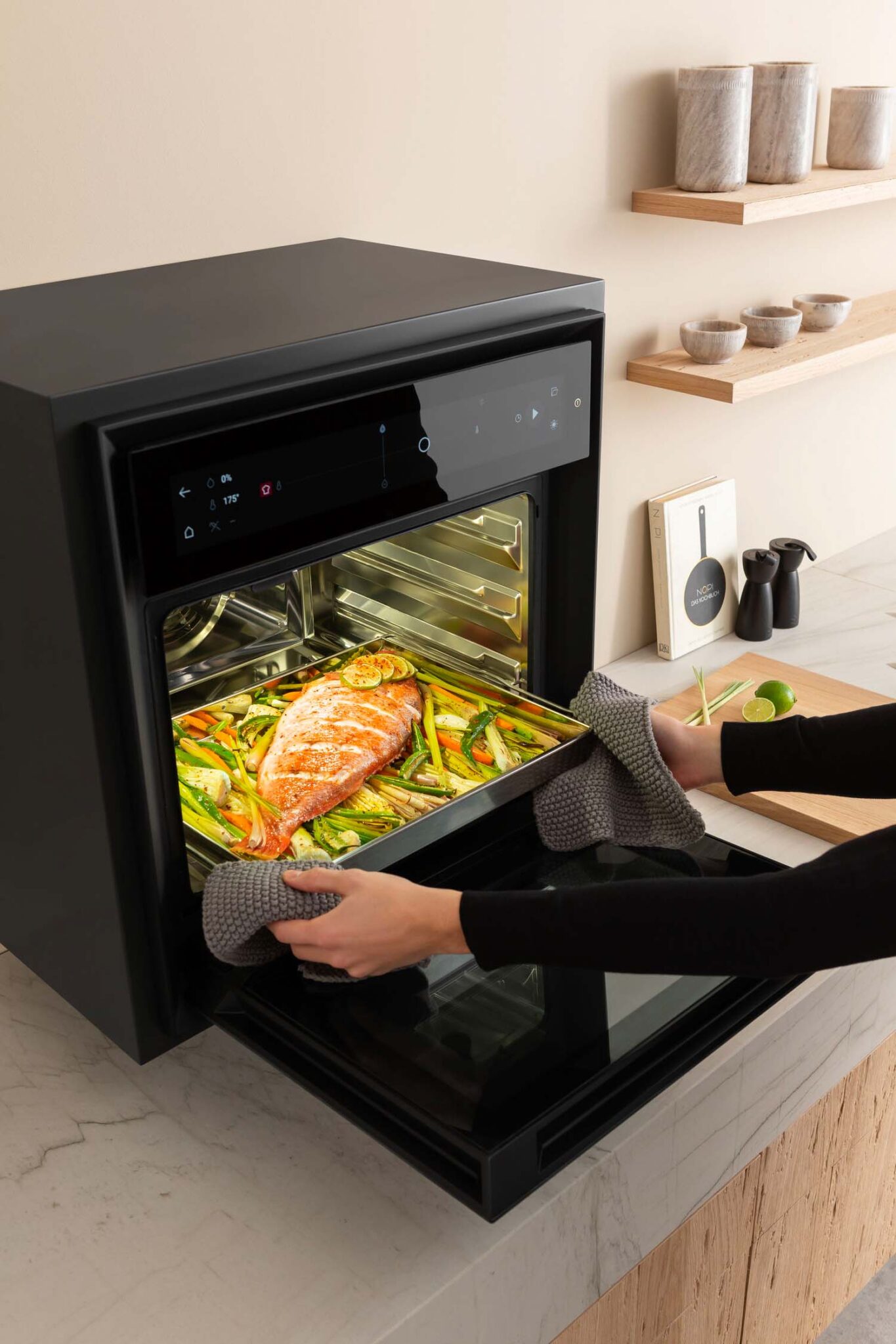 Person loading vegetables into BORA X BO steam oven with triple-level trays and large touchscreen display.