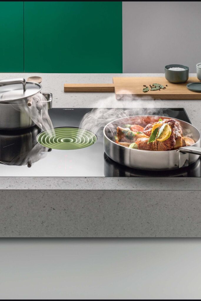 Vegetables cooking in a silver pan on a BORA Pure hob against a green background.
