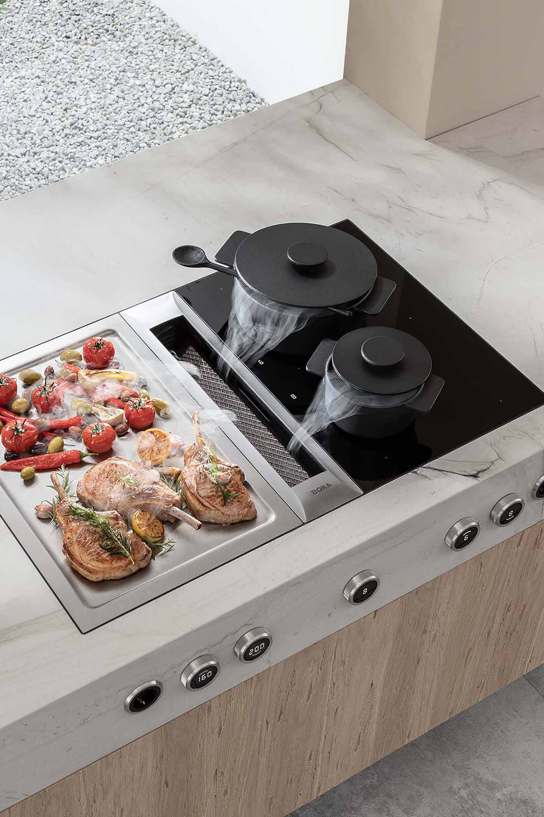 BORA Professional cooktop configuration: left-side induction zone hosts a cast-iron oven releasing steam, while the right stainless teppanyaki grill plate sears two herb-topped salmon fillets alongside asparagus, fennel wedges and mushrooms; a hand adjusts the illuminated touch slider beneath the central extractor grille.