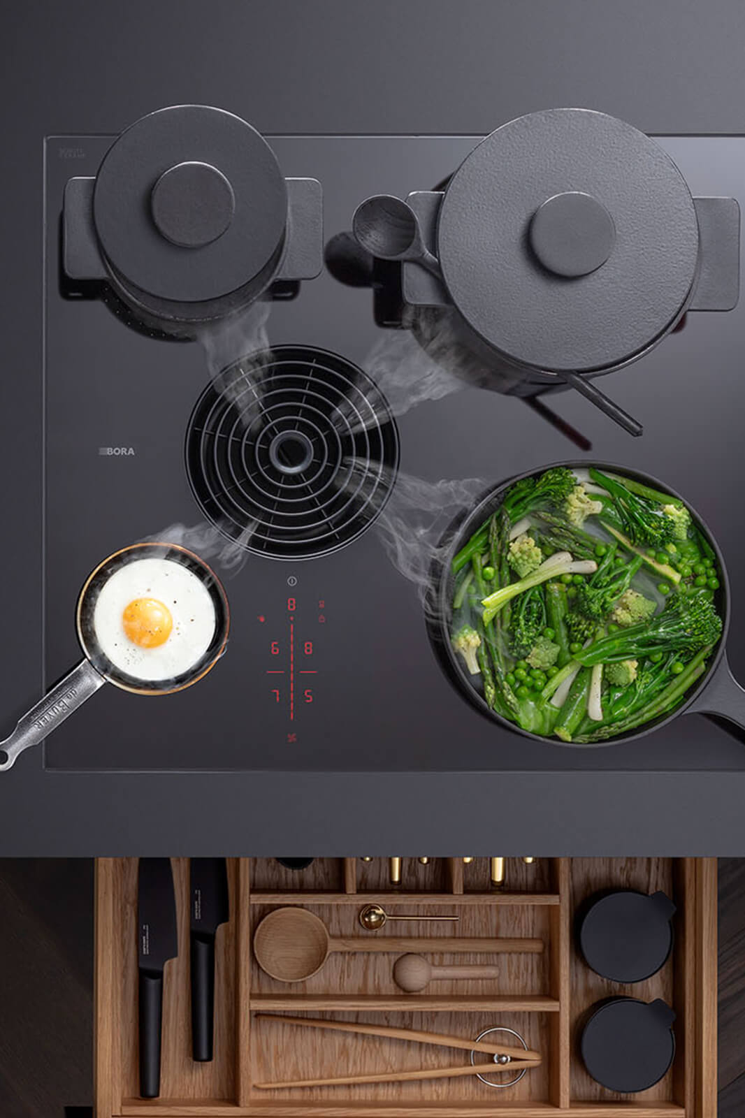 Minimalist overhead view of a BORA S Pure cooktop: four flush cooking zones radiate from the central square vent, framed by warm timber cabinetry and accented with a small potted plant for a clean, architect-designed aesthetic.